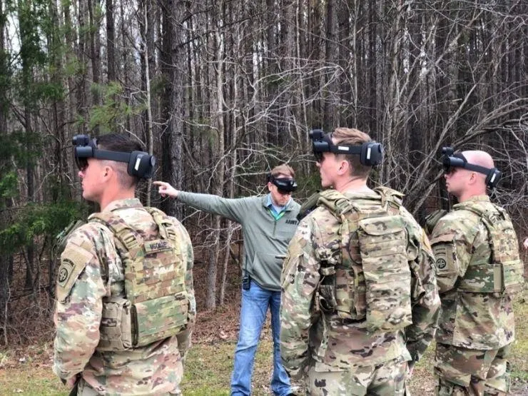 Military personnel in tactical gear training in a forested area.