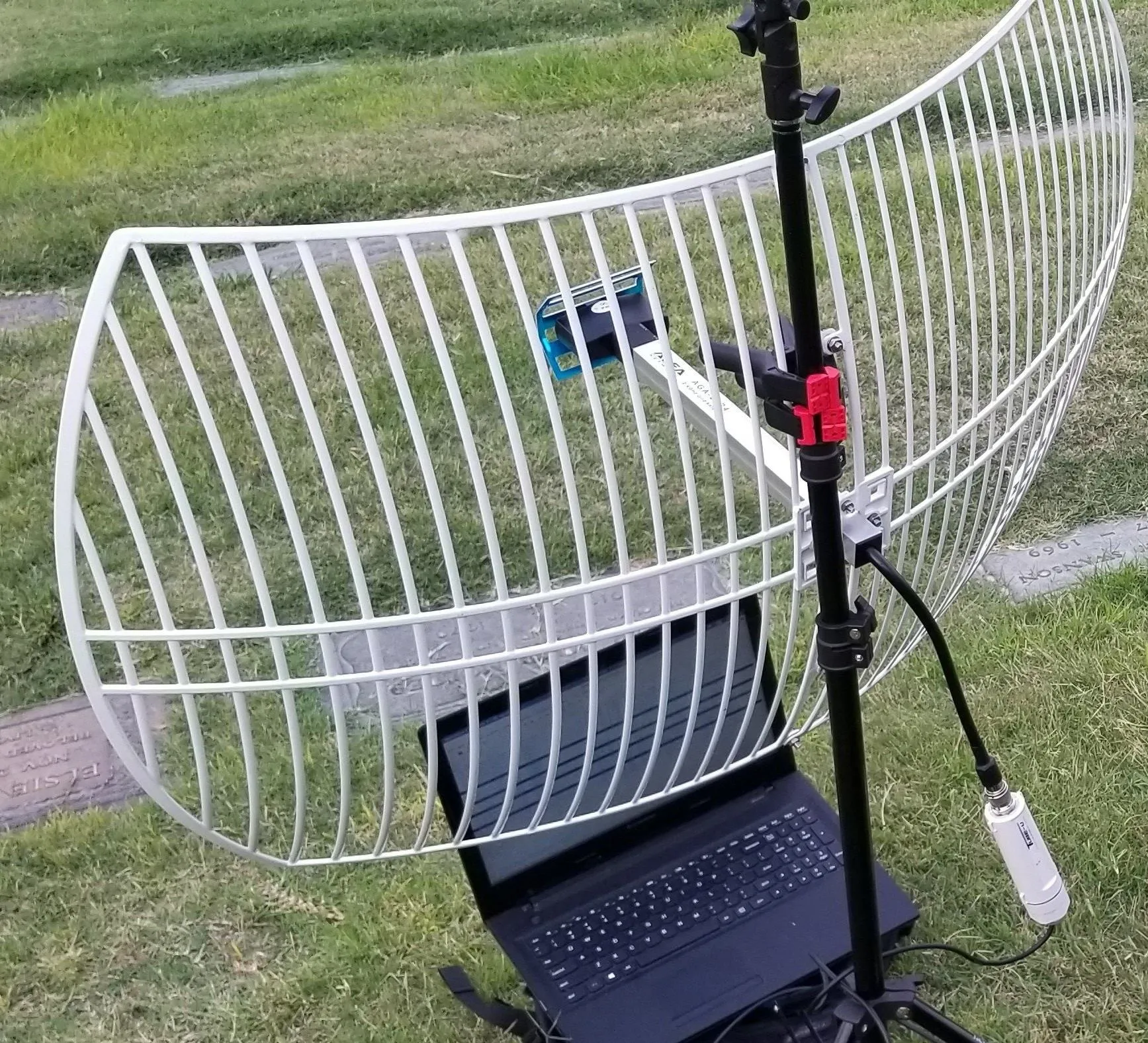 A setup featuring a large white antenna on a stand with a laptop underneath, positioned outdoors on grass.