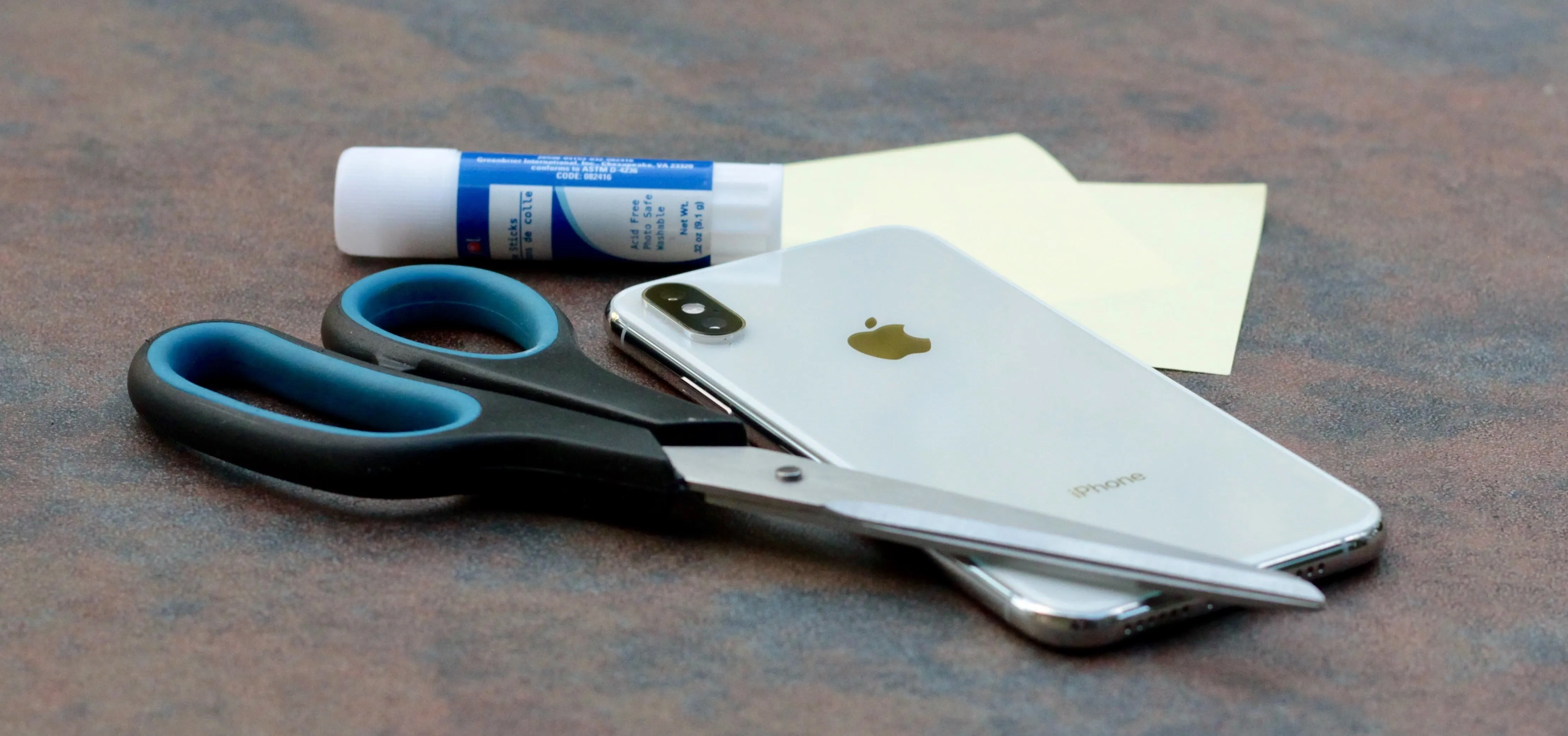 Office supplies including scissors, a smartphone, a glue stick, and sticky notes.