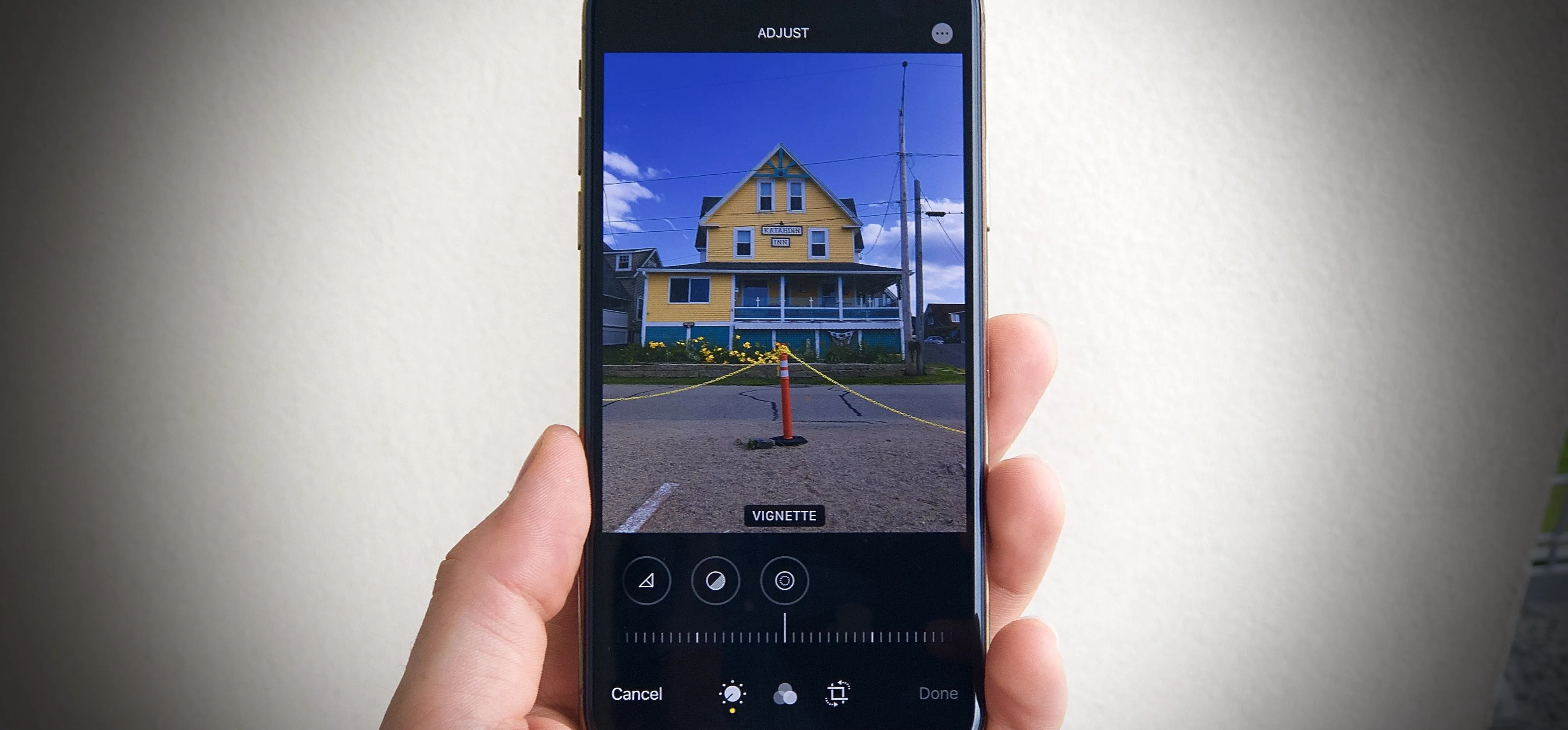 A person holding a smartphone displaying a photograph of a yellow house with a traffic cone in front.