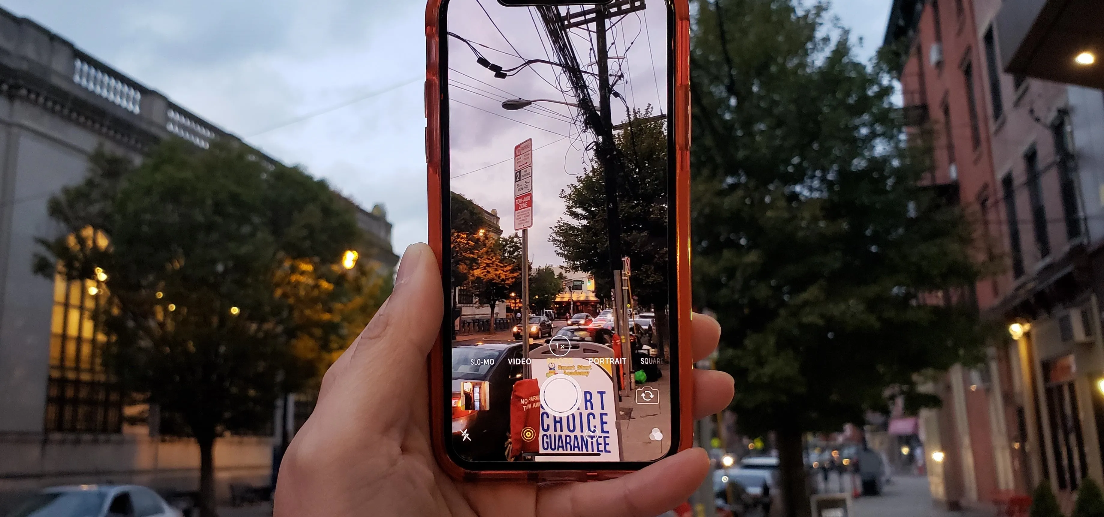 A person holding a smartphone displaying a street scene with trees and a traffic signal.