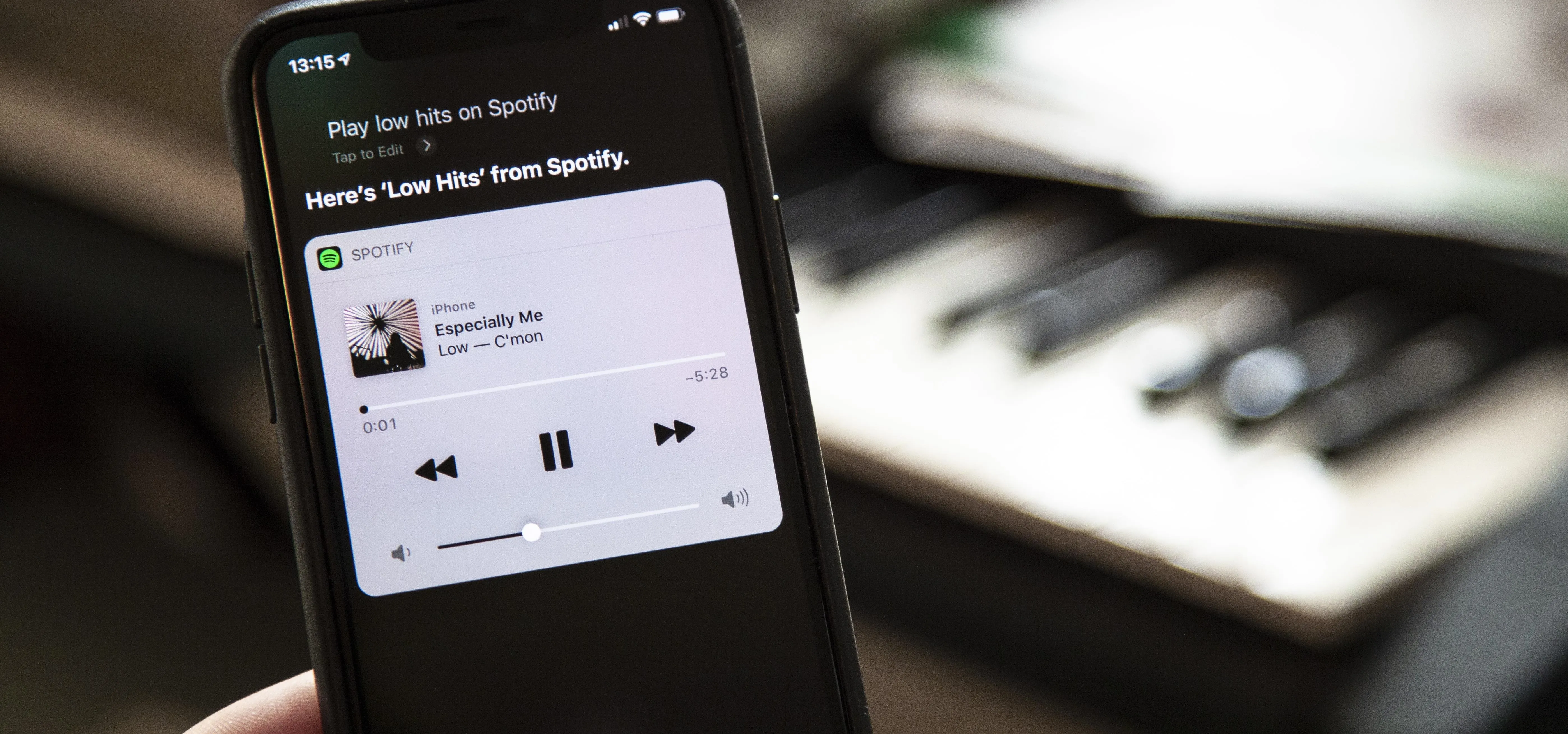 Smartphone displaying playback controls for Spotify with a blurred keyboard in the background.