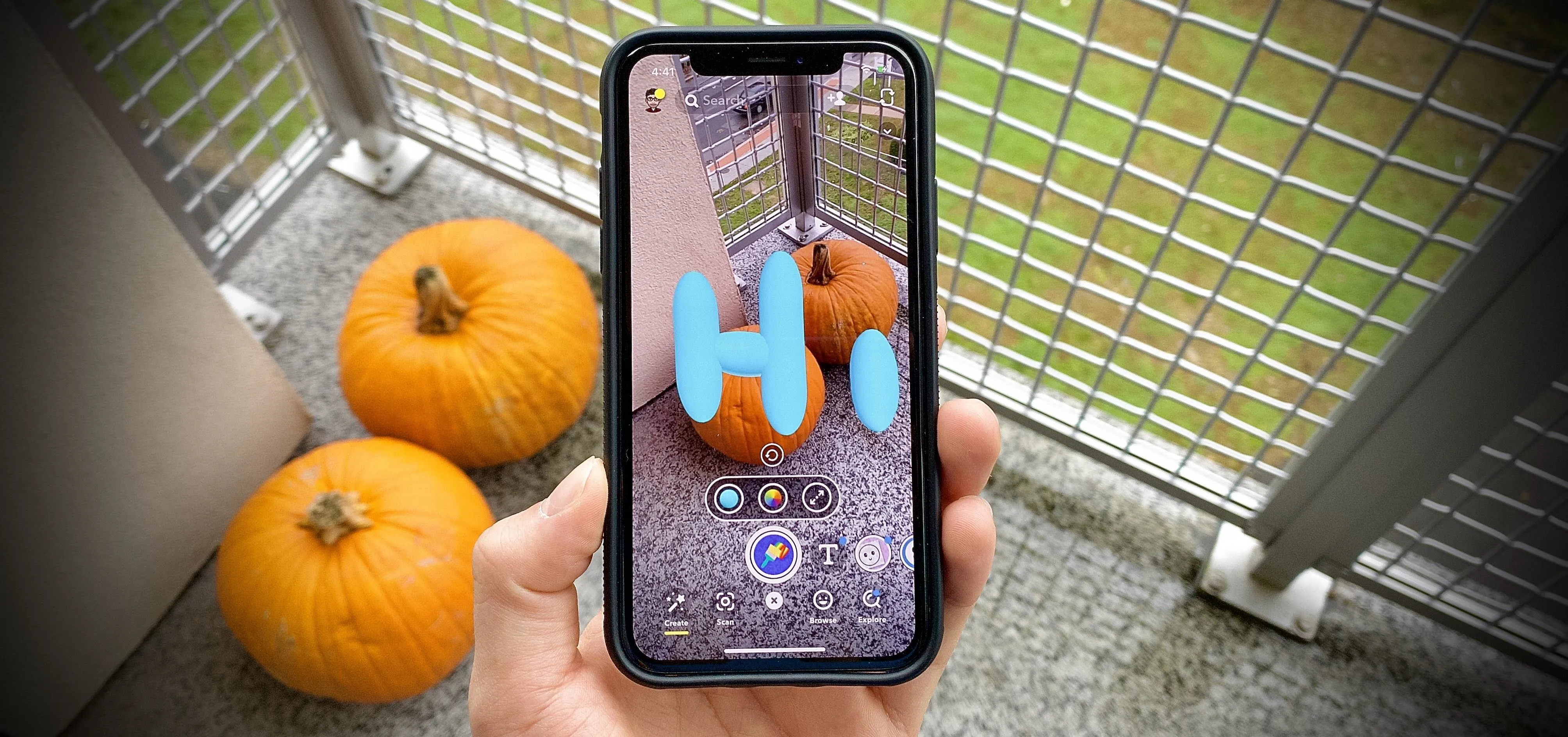 Person holding a smartphone displaying augmented reality with pumpkins in the background.