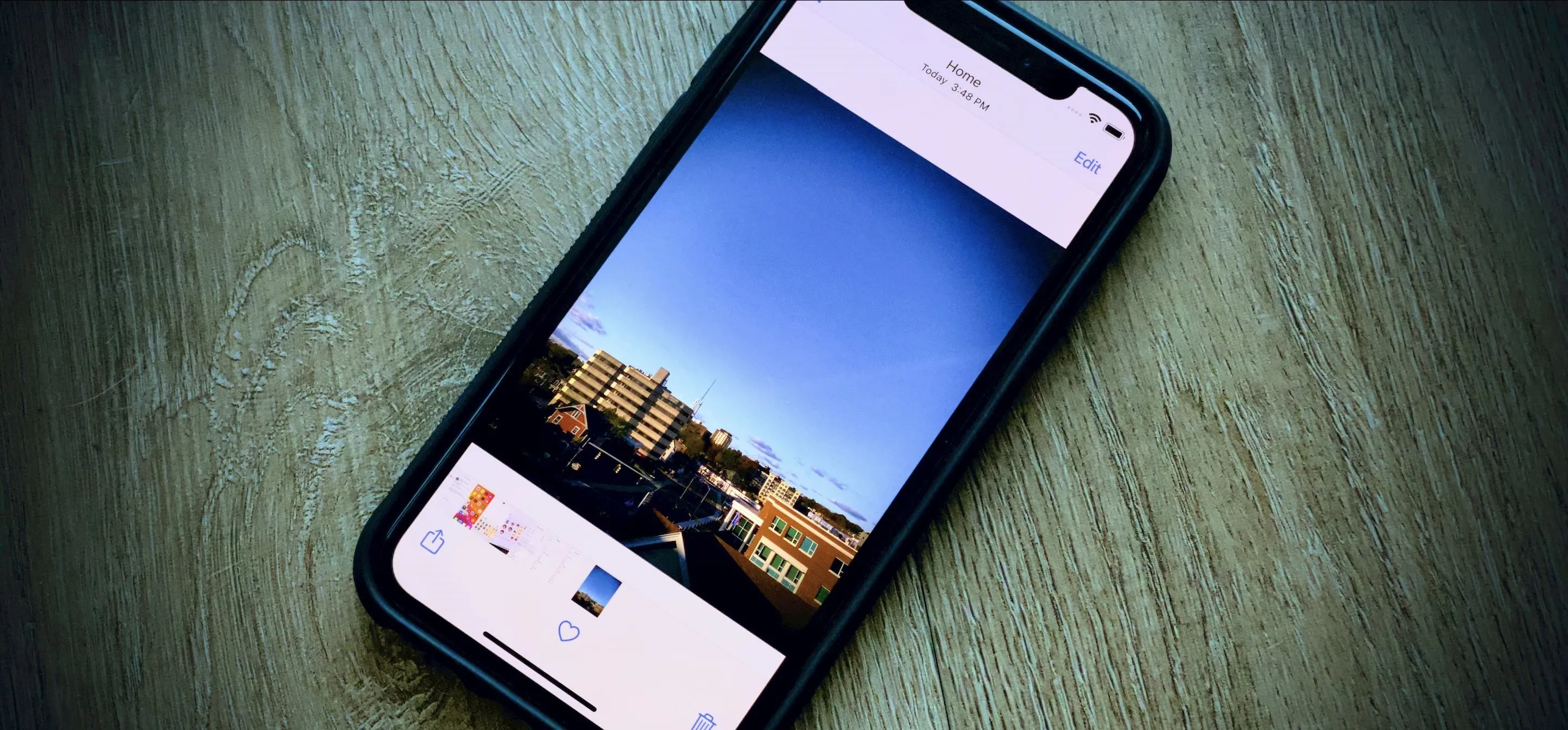 Smartphone displaying a clear blue sky and buildings on a wooden surface.