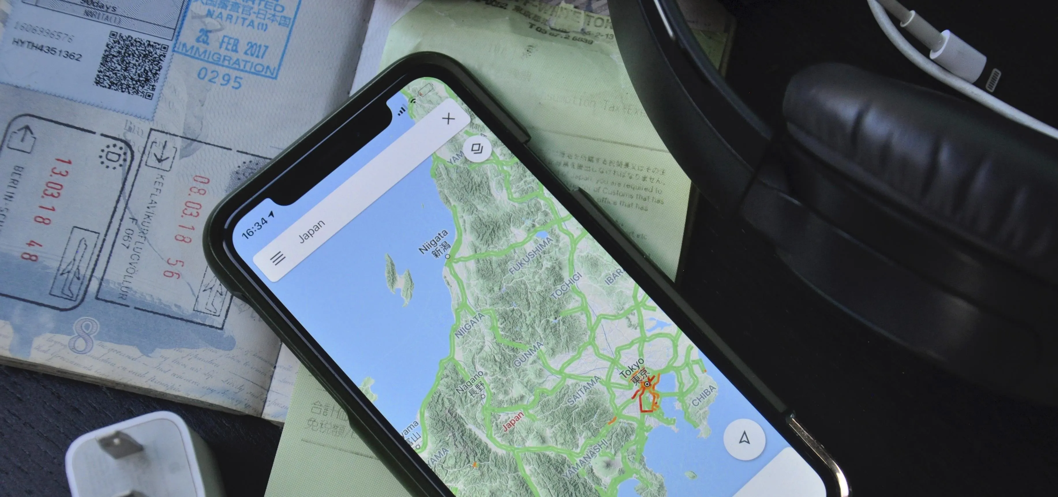 Smartphone displaying a map on a table with travel documents and headphones.