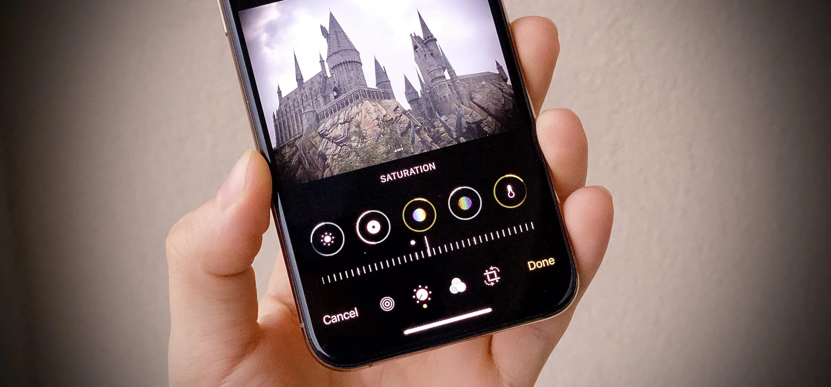 A hand holding a smartphone displaying a photo of a castle with editing options visible below.