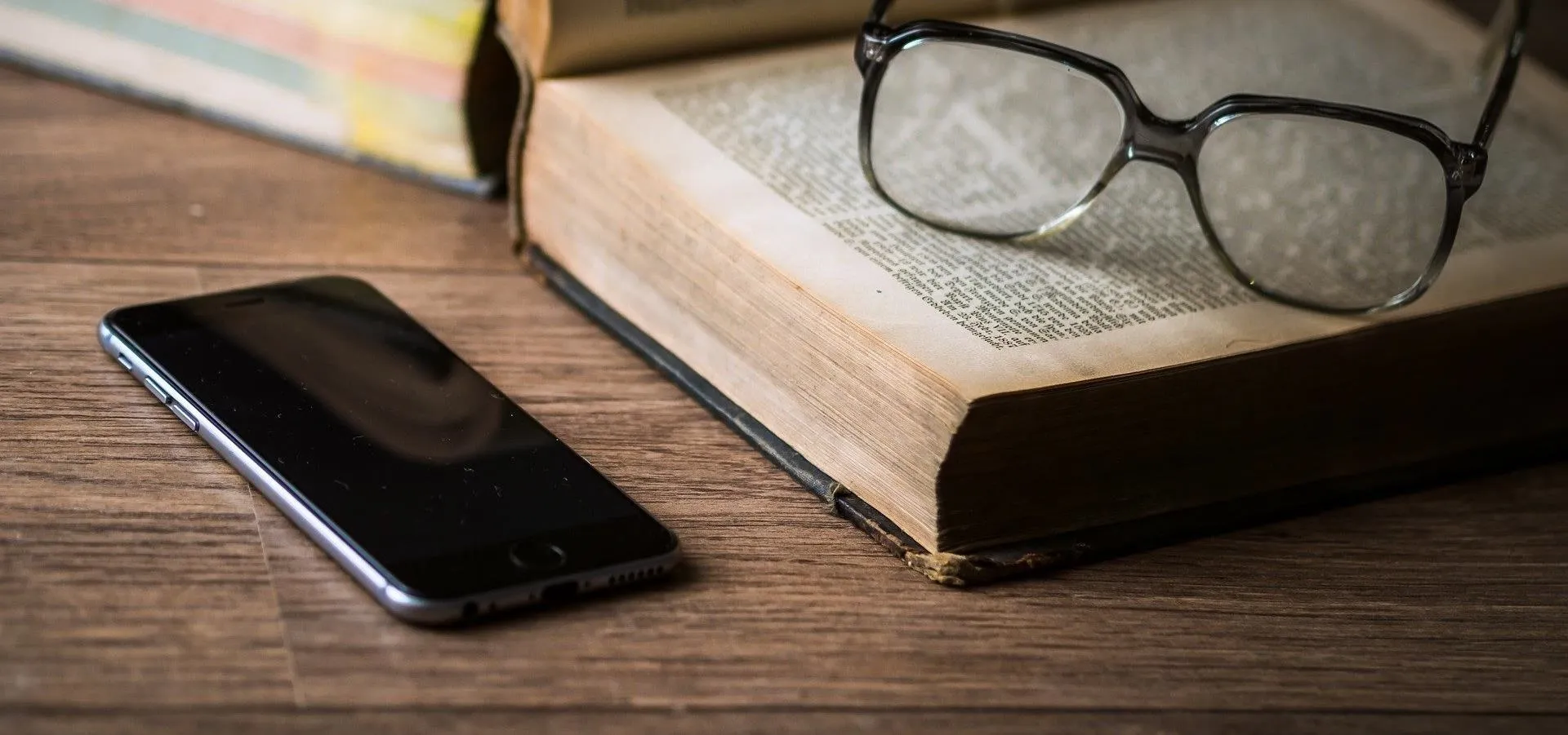Glasses and a smartphone on a wooden table next to an open book.