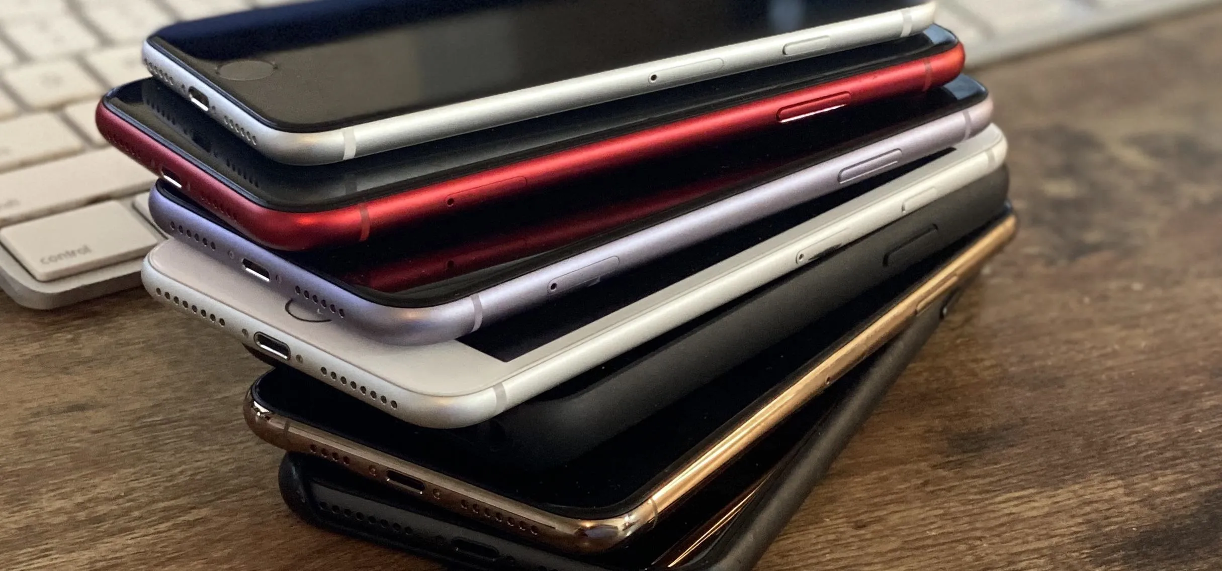 Stack of smartphones in various colors on a wooden surface.