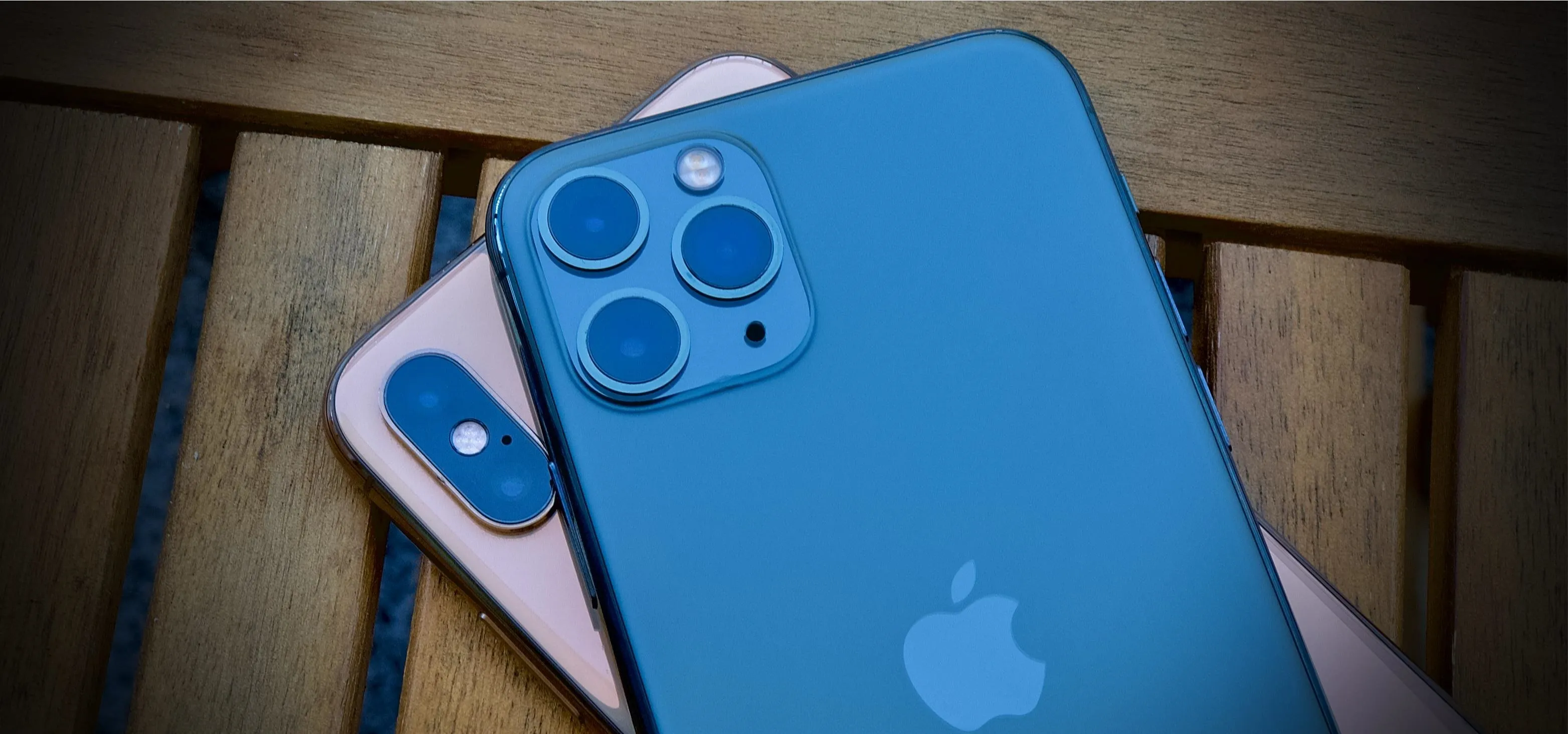 Two smartphones, one blue and one pink, resting on a wooden surface.