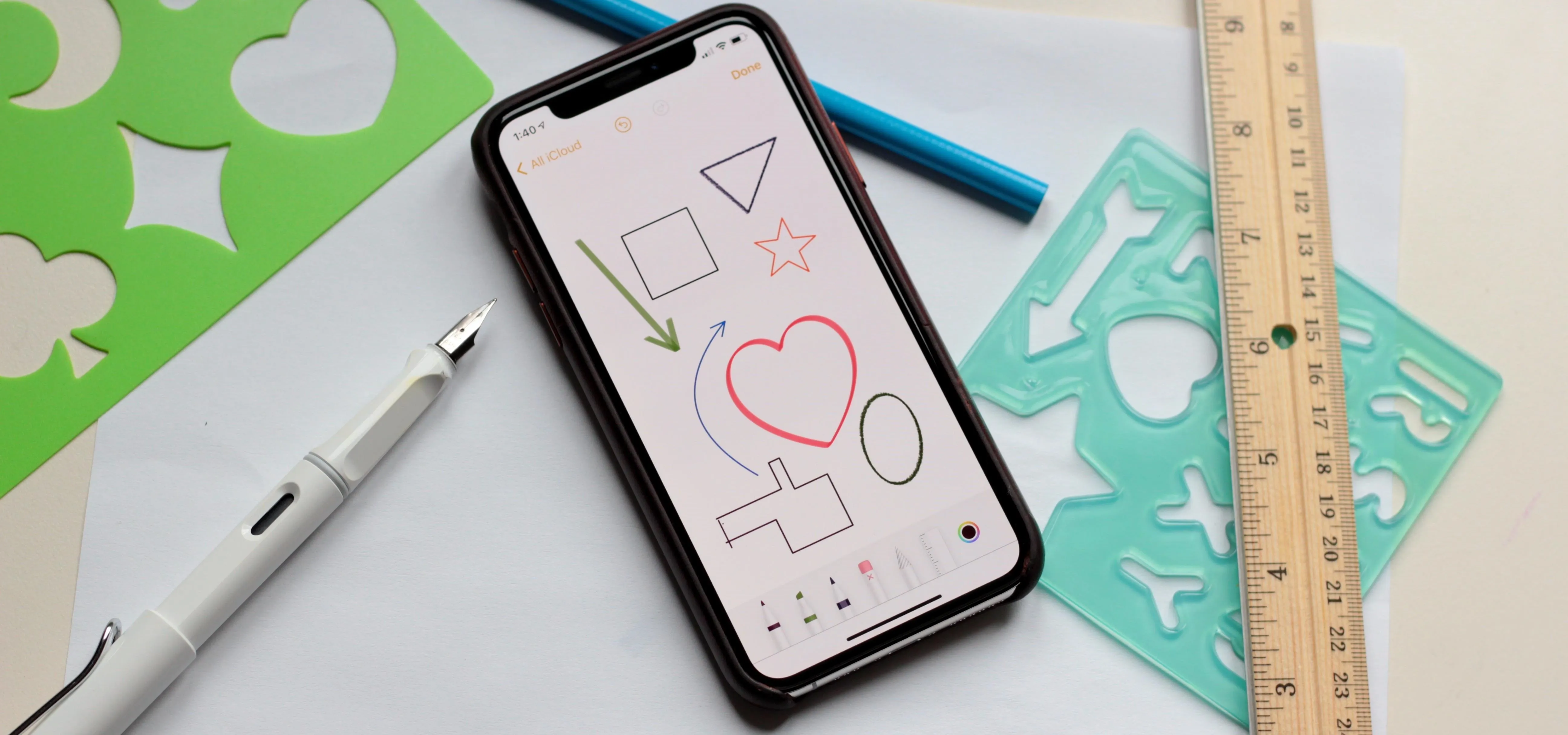 Smartphone displaying drawn shapes alongside stationery items.