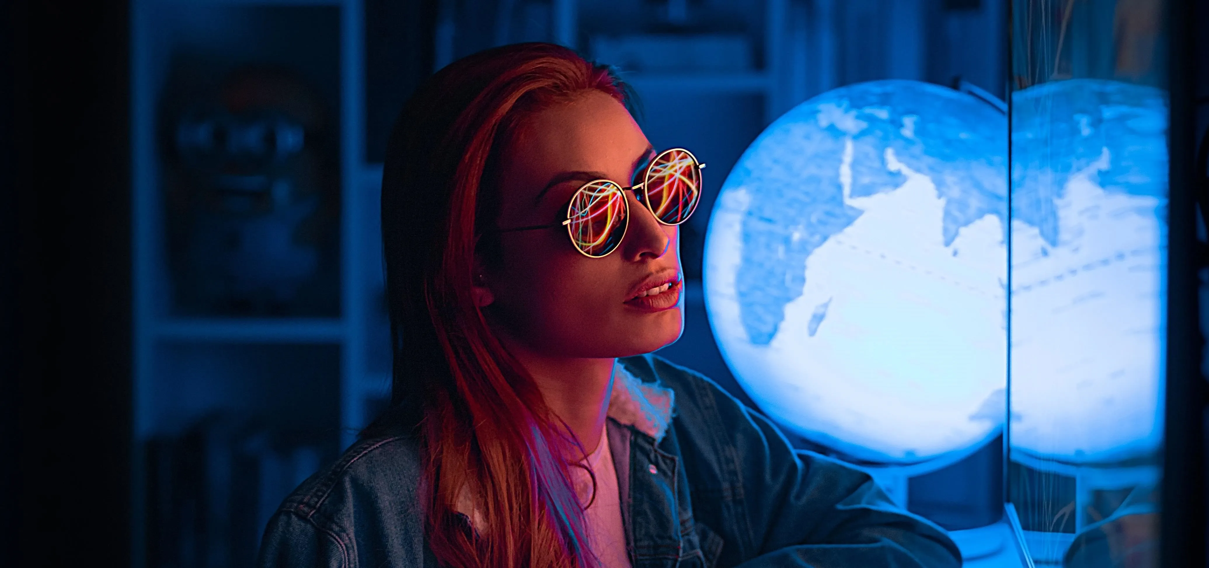 Young woman in stylish sunglasses near a glowing globe in a dark room.