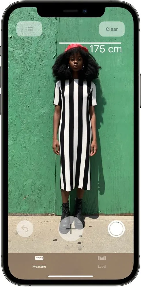 A woman in a striped dress standing in front of a green wall, with a measurement tool displayed on the phone screen.