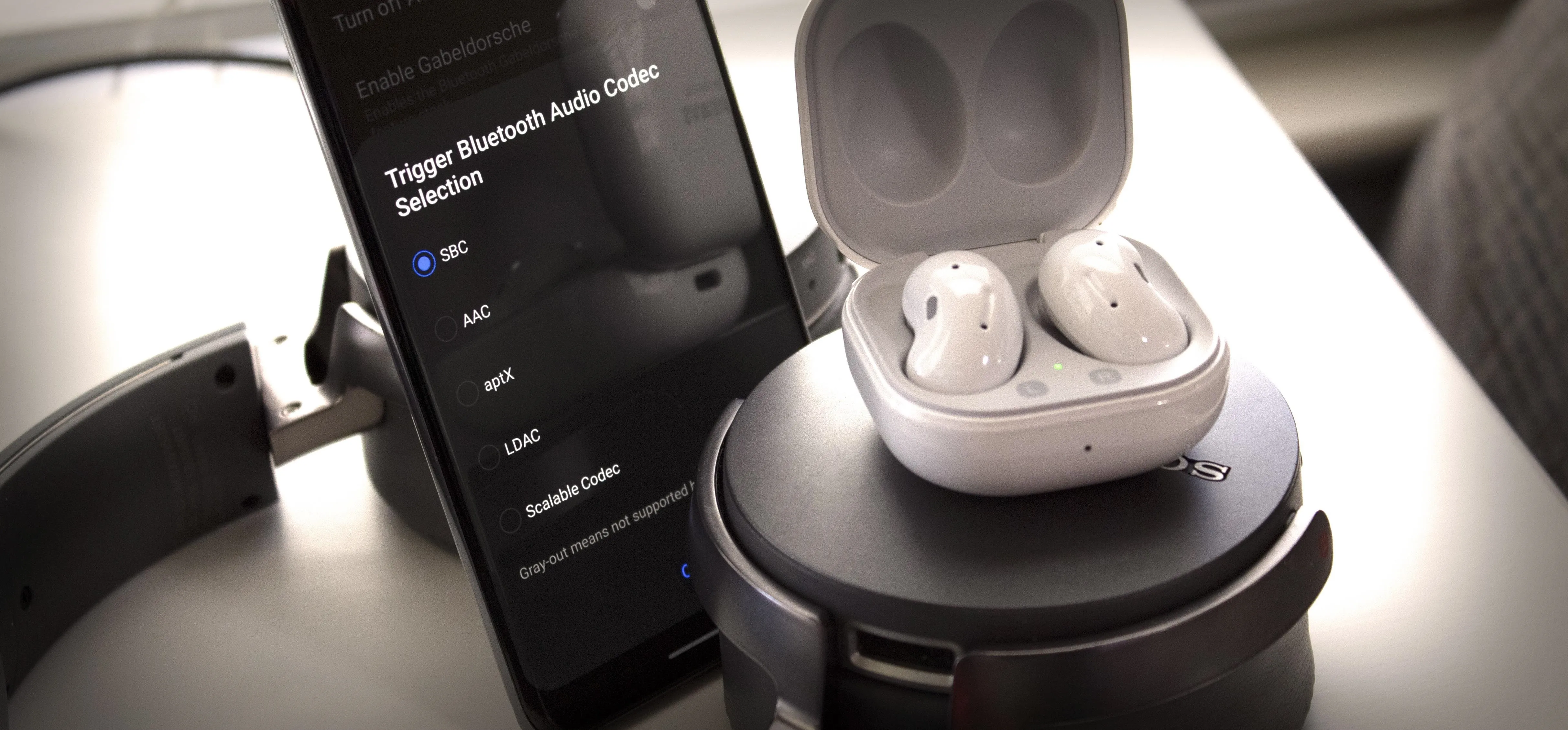 Wireless earbuds in charging case next to a smartphone displaying audio settings.