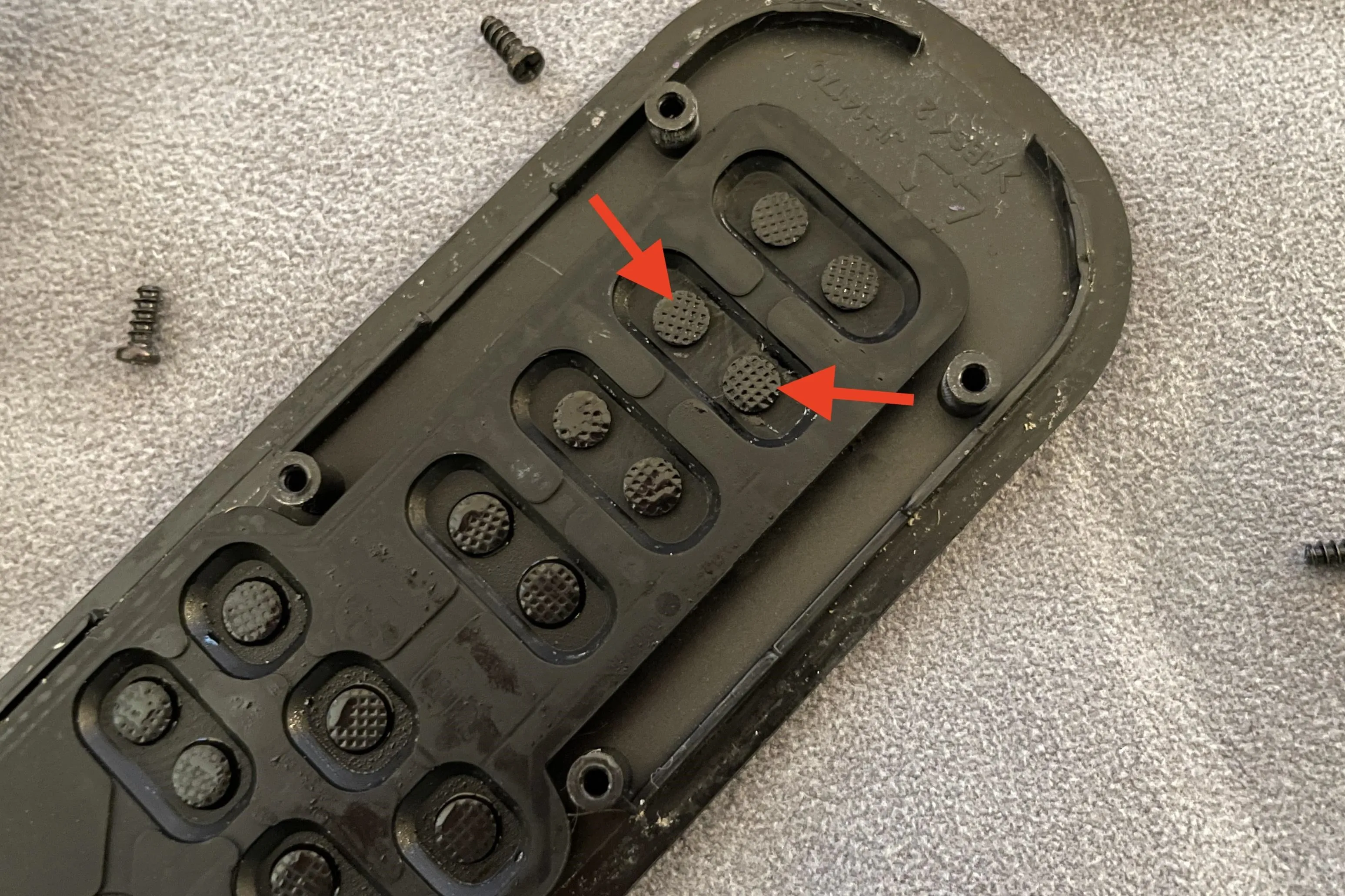 Close-up of a black remote control casing with arrows pointing to a button and screws.