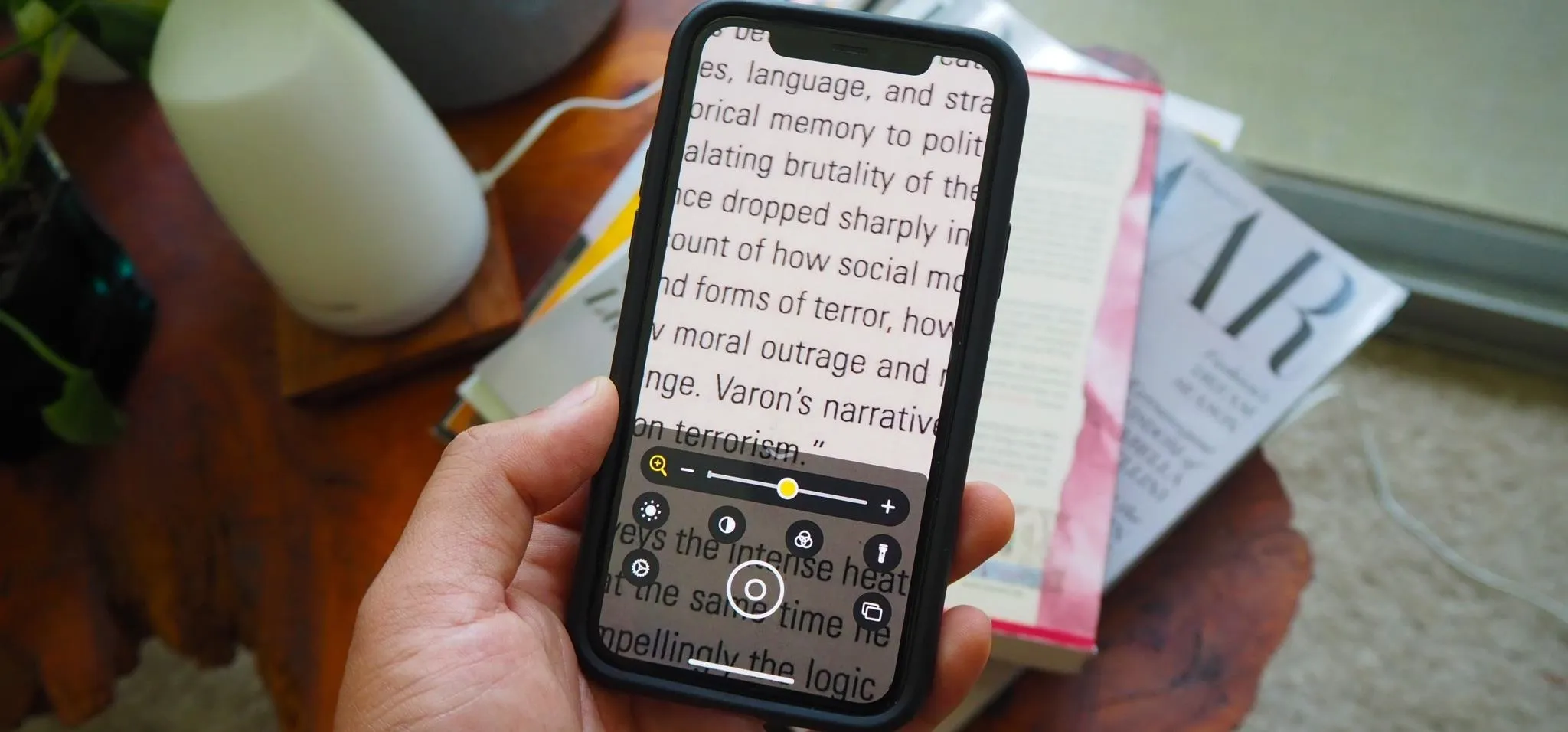 A person holding a smartphone displaying text recognition features with books in the background.