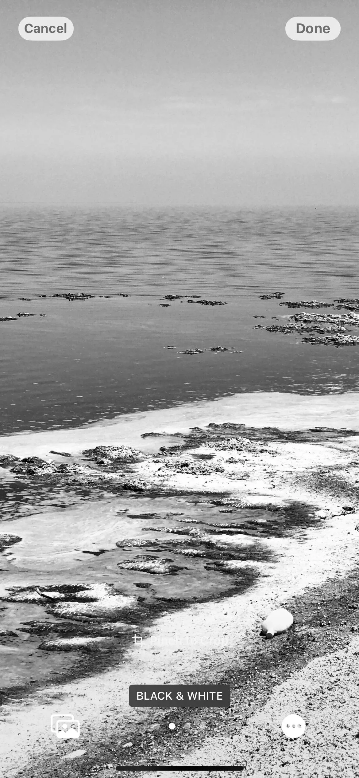 Black and white seascape with rocky shoreline and calm water.