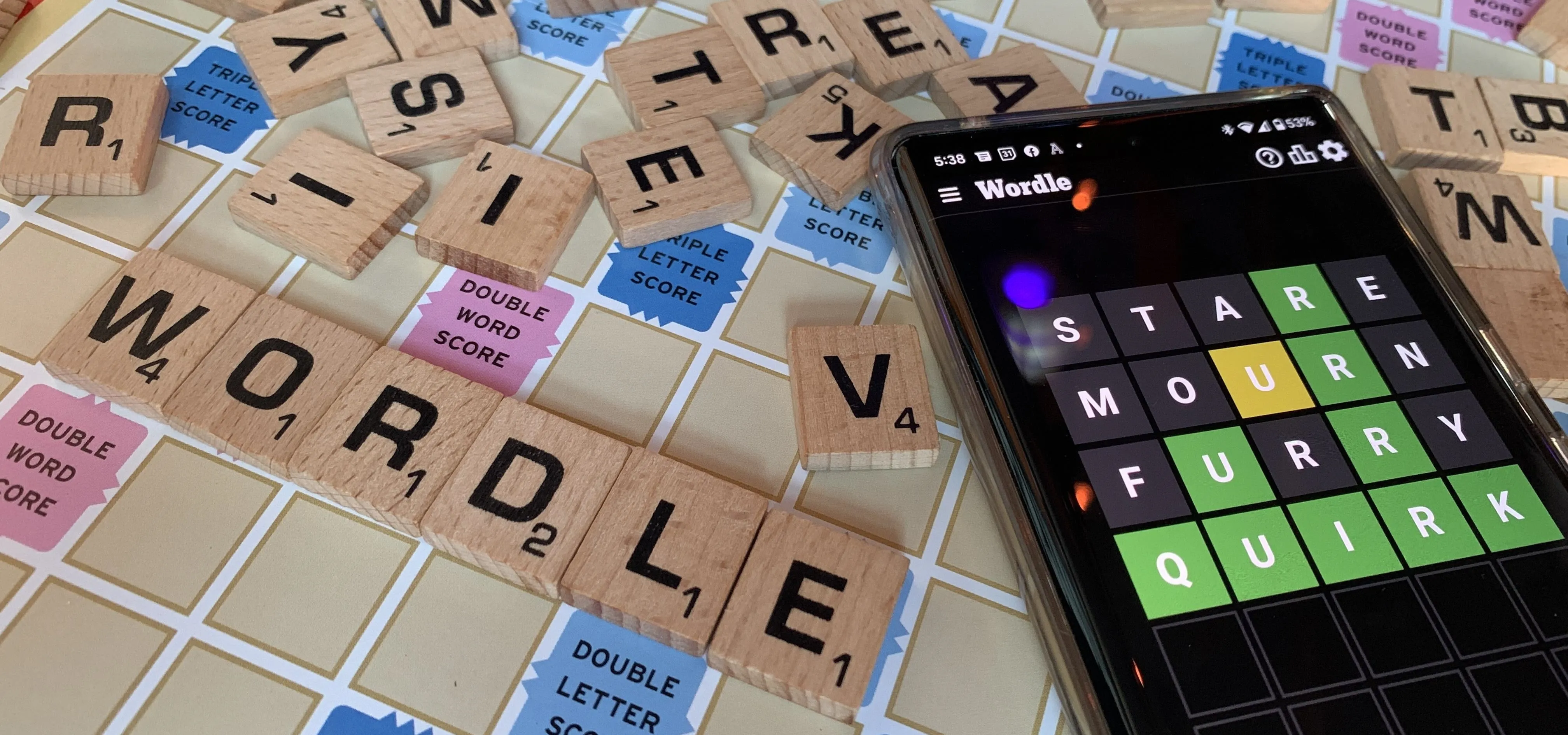 Wordle game displayed on a smartphone with Scrabble tiles in the background.