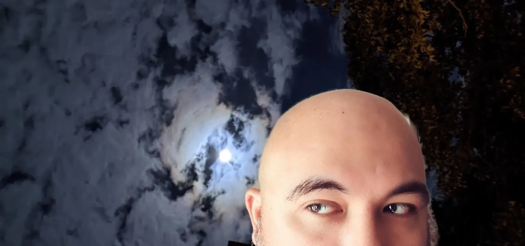 A person's head against a cloudy night sky with a visible moon.