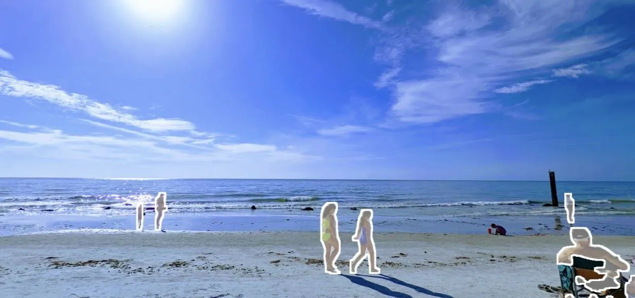 People walking along a sunny beach with a clear blue sky.