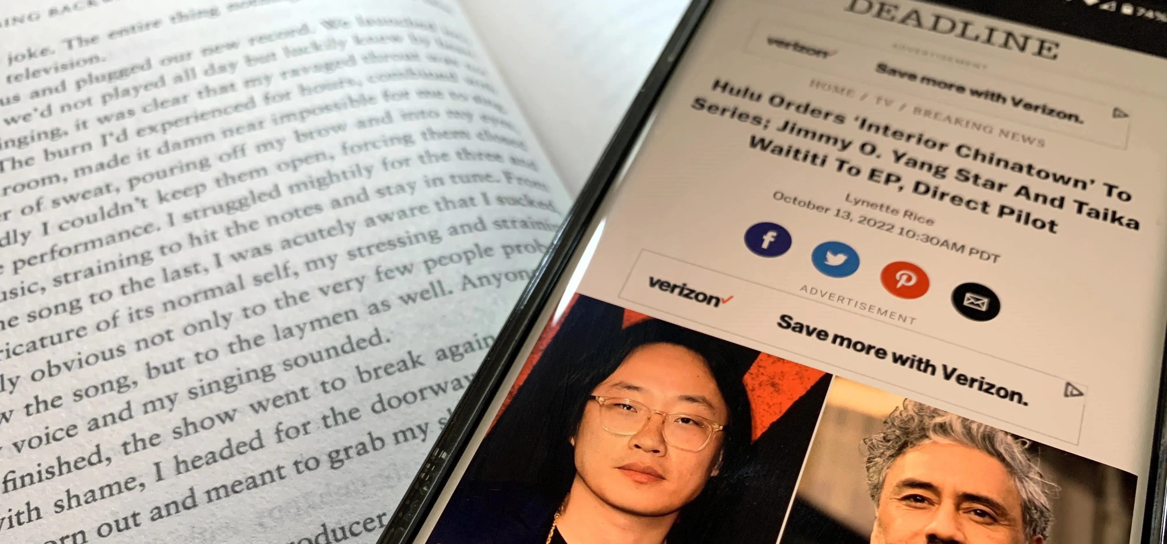 Mobile phone displaying an article from Deadline next to an open book.