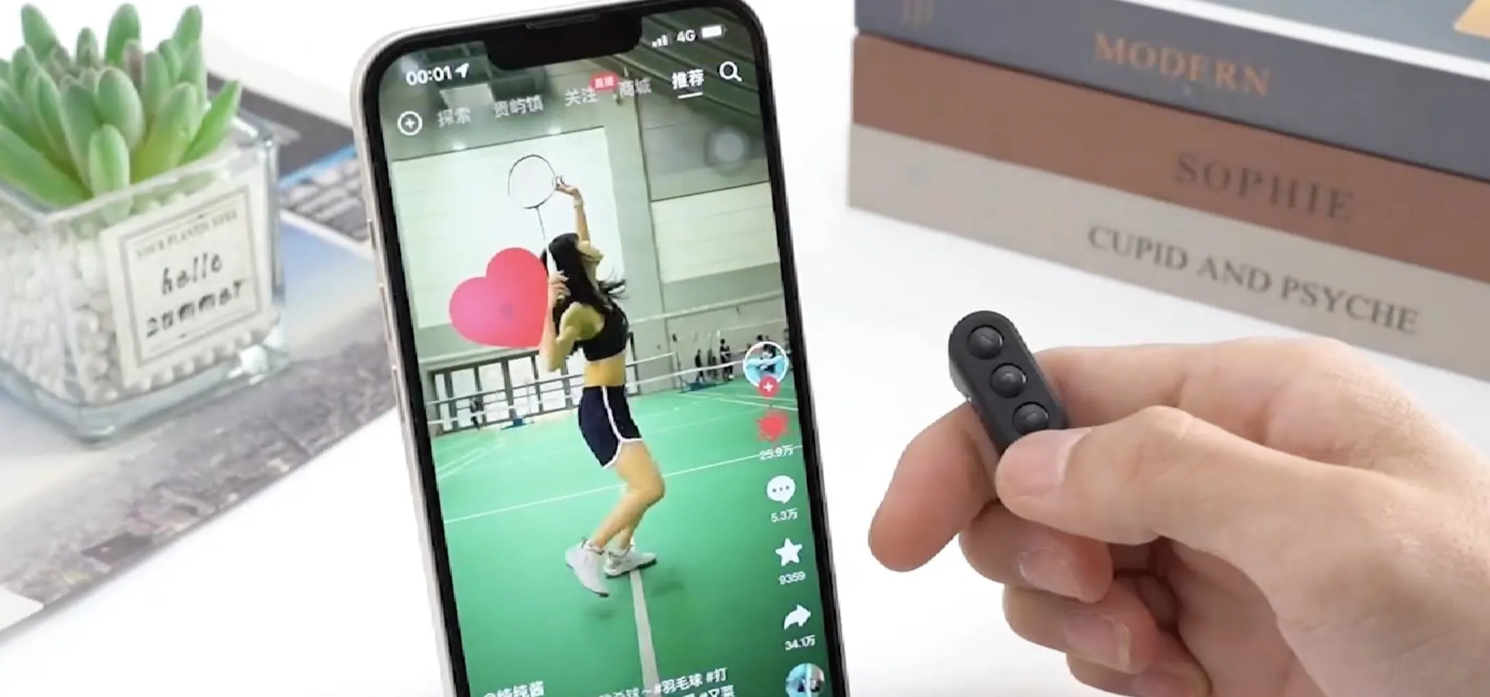 Person using a smartphone to record a video, with a remote control in hand, while showcasing a dance move on a green court.