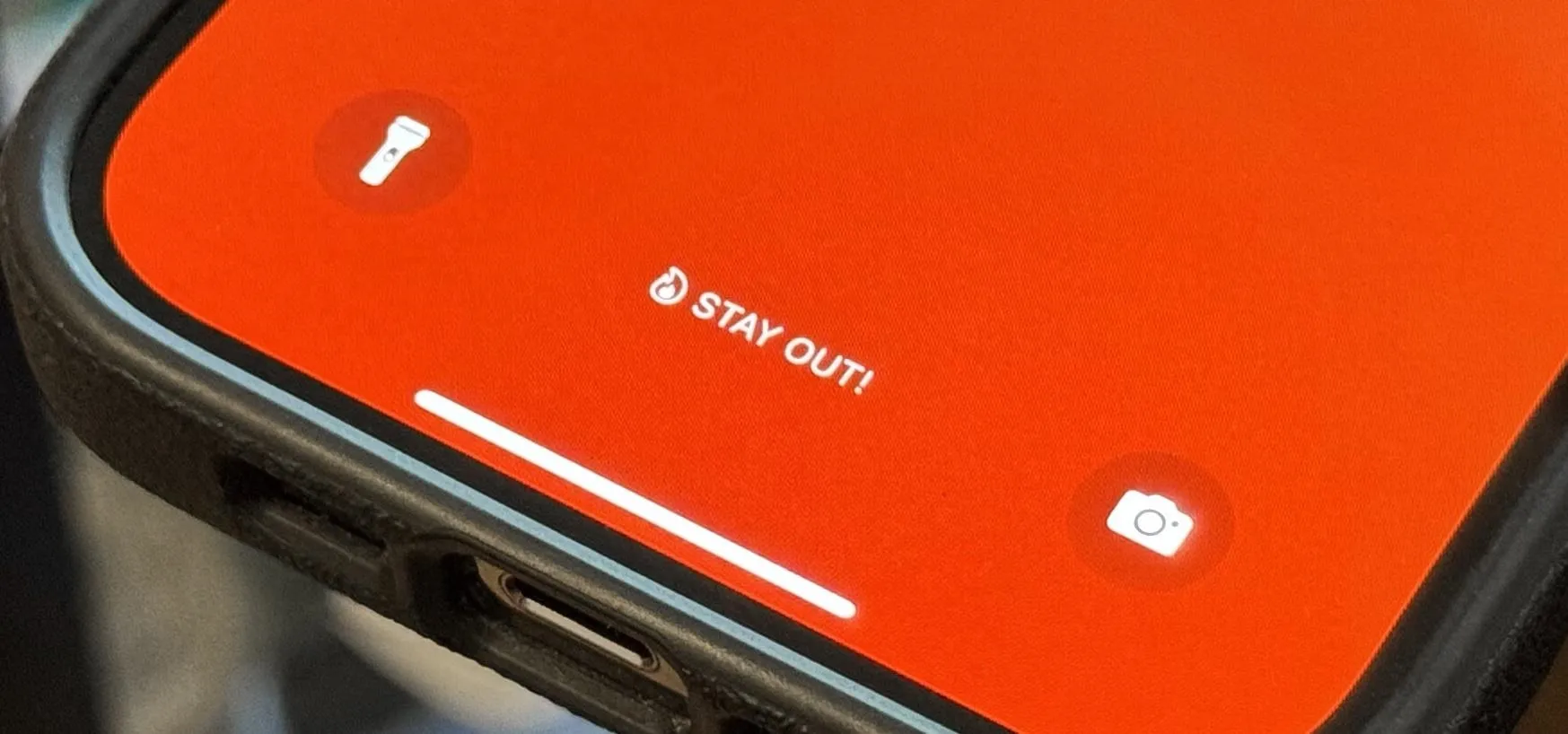 Smartphone interface displaying a red background with icons for flashlight and camera, and the text "STAY OUT."