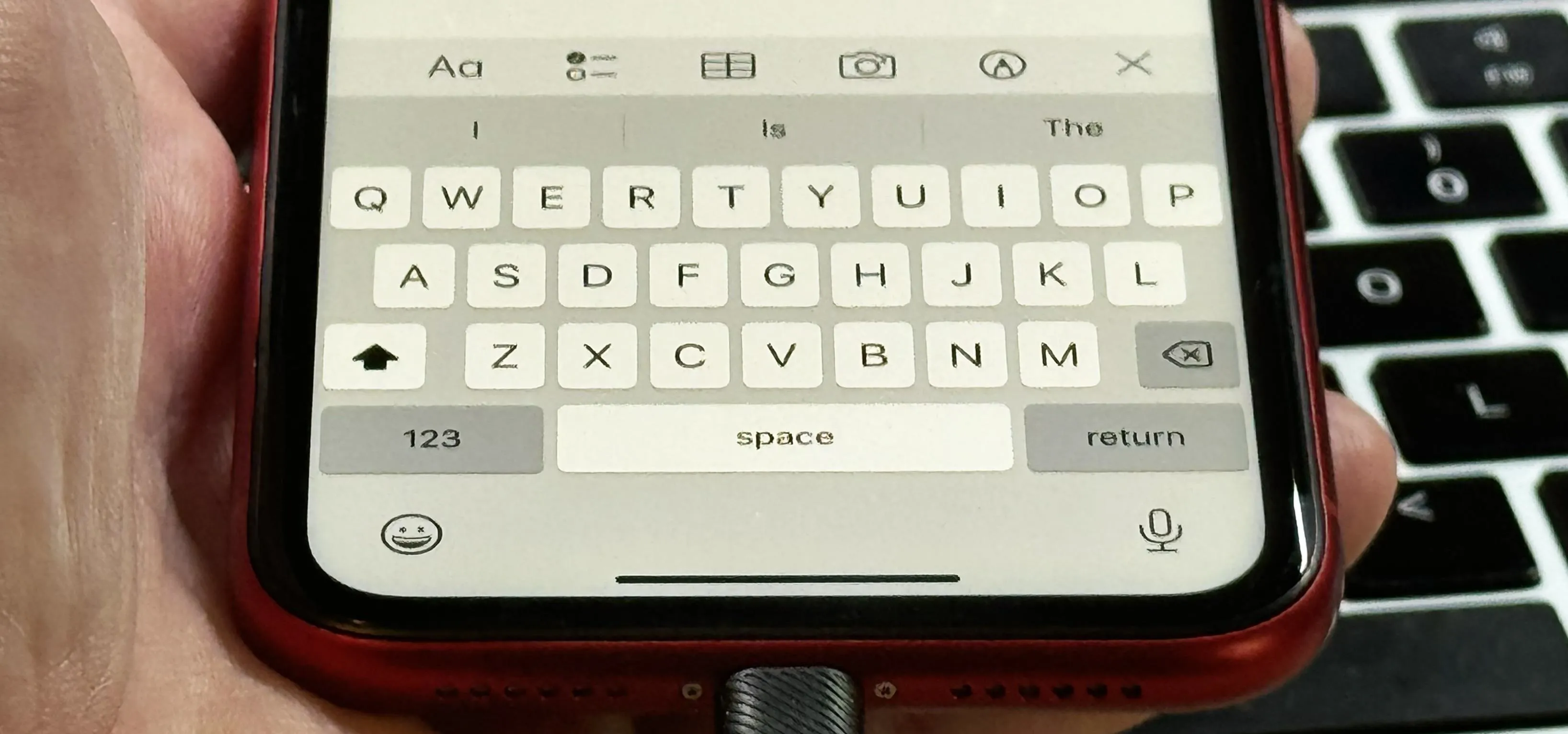 Smartphone keyboard displayed on device with a laptop in the background.