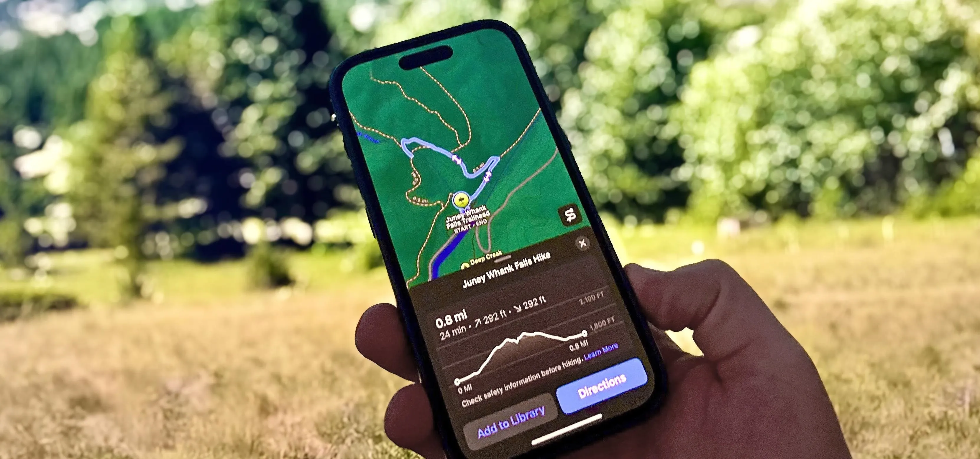 Person holding a smartphone displaying a map with navigation details in a natural outdoor setting.