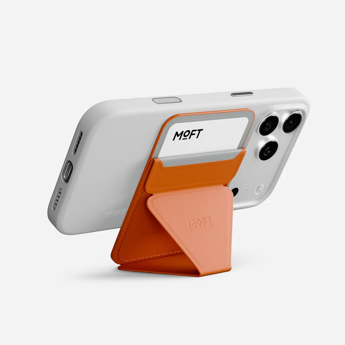 MOFT Trackable Snap-on MagSafe Wallet in orange, attached to an iPhone and folded into a landscape phone stand