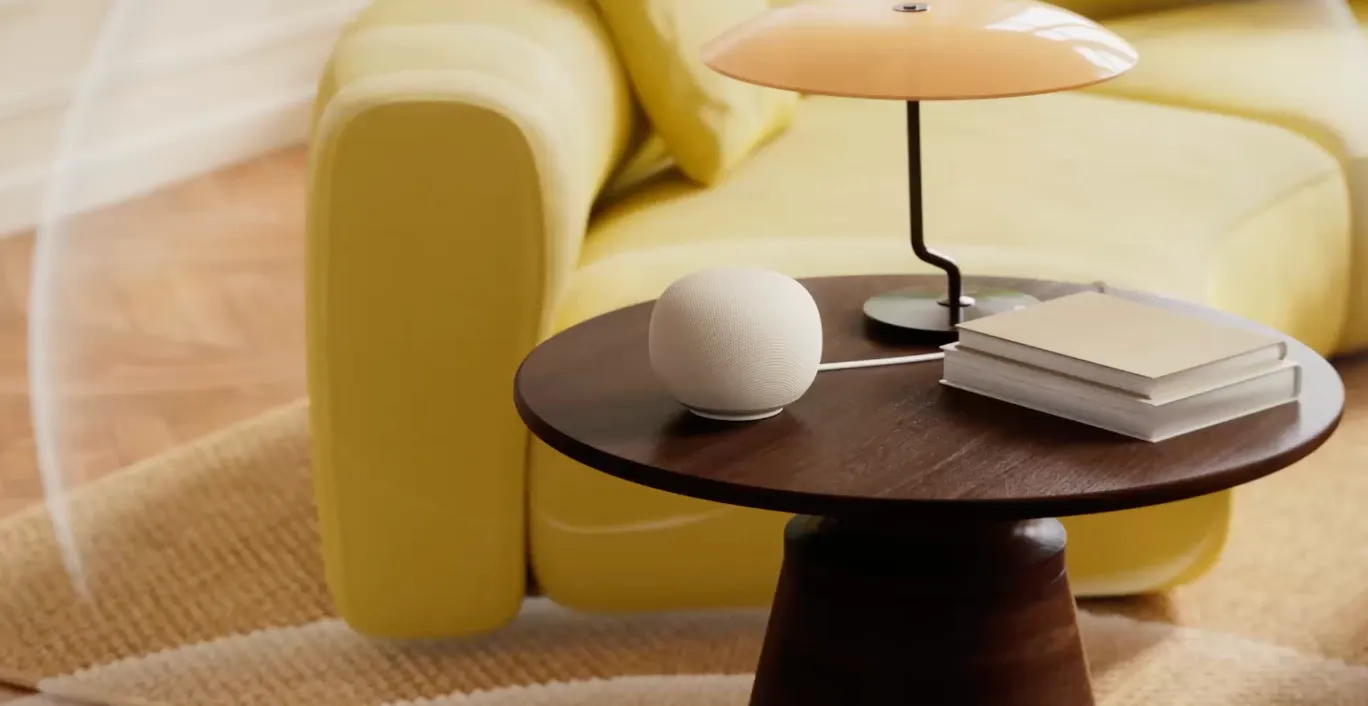 Google Home Speaker on a dark wood side table beside a lamp and yellow sofa