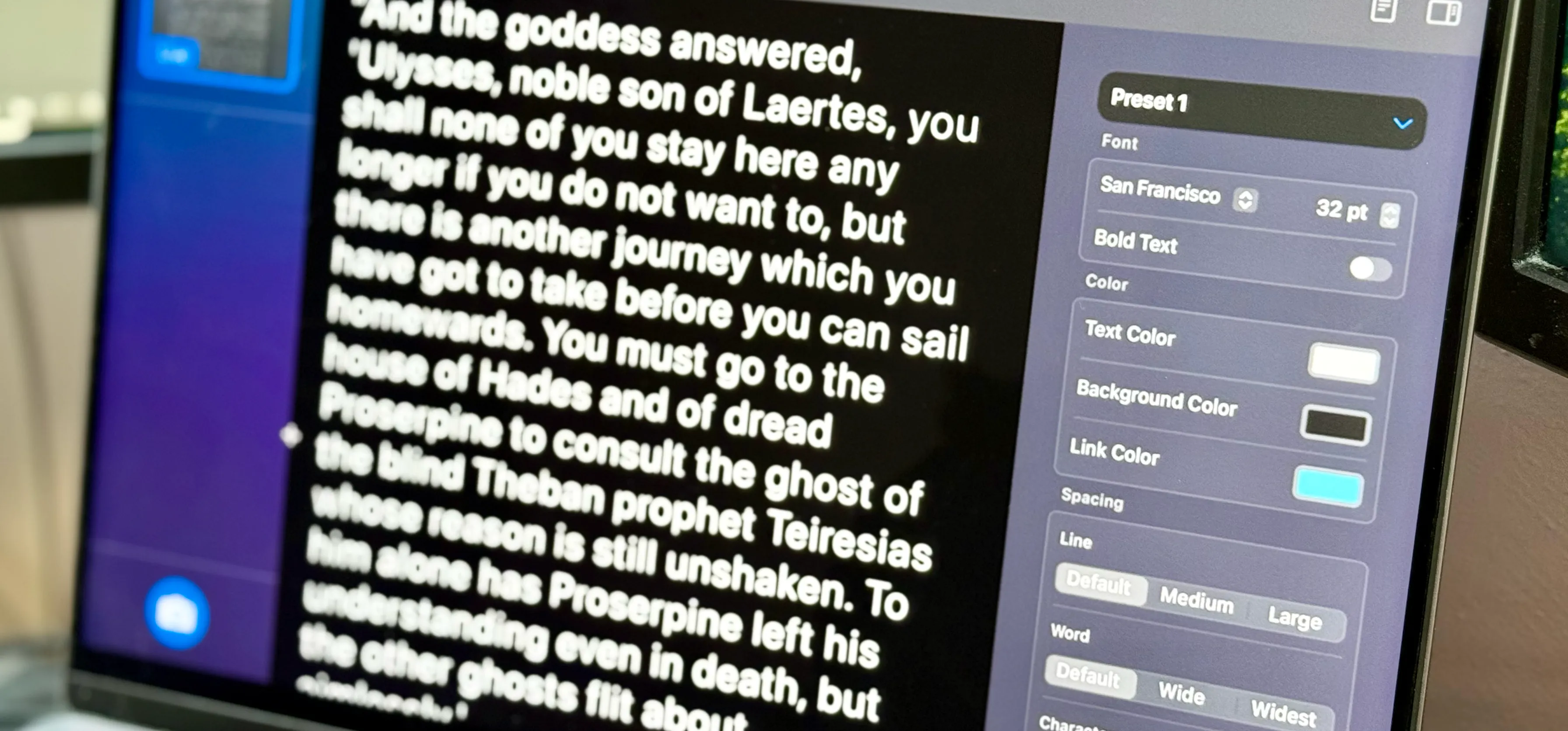 MacBook screen tilted, Accessibility Reader displays enlarged white text on black background, sidebar reveals font, color, and spacing controls.