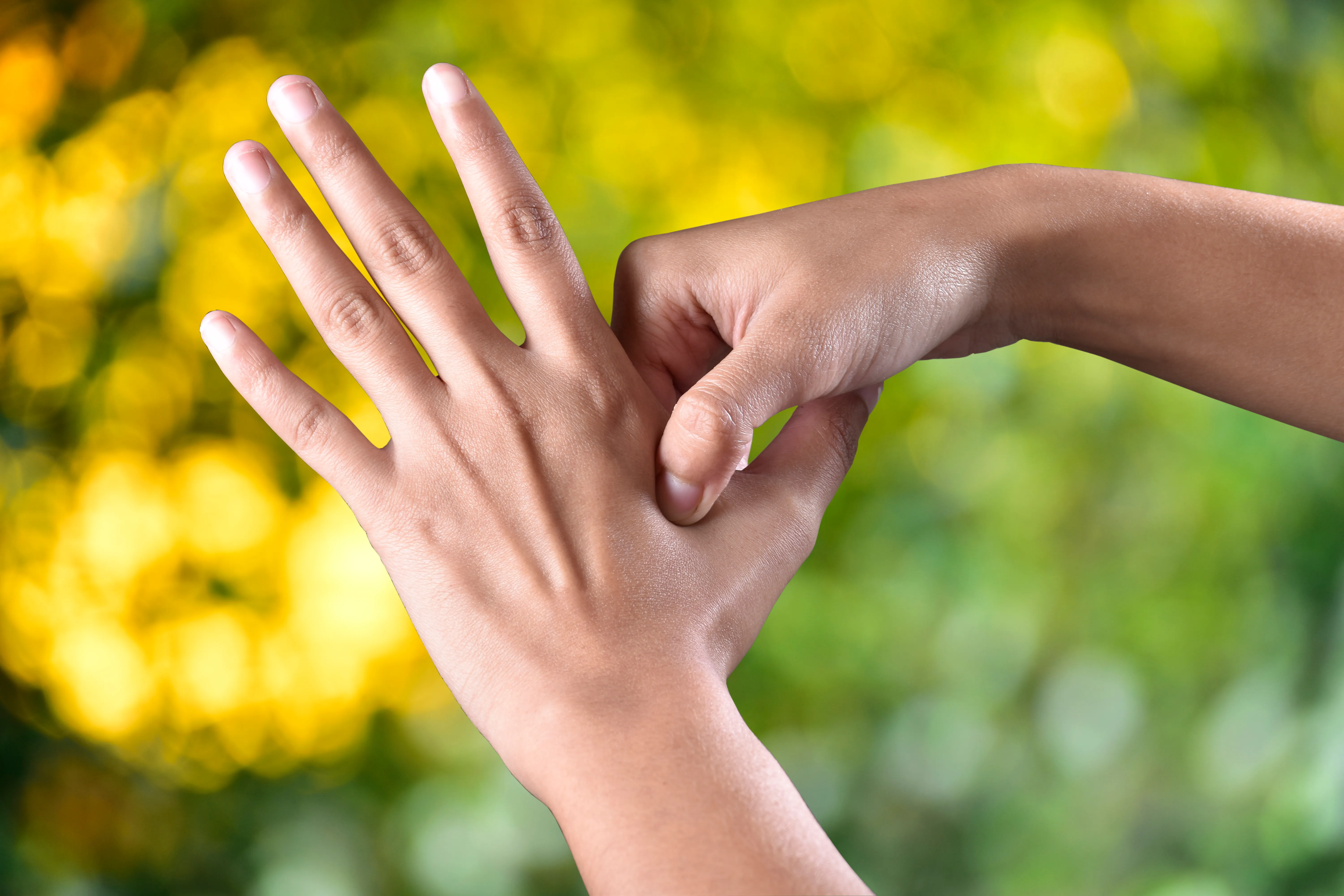 A hand shown with its palm facing away with fingers spread out and another hand squeezing the open hand between thumb and index finger.