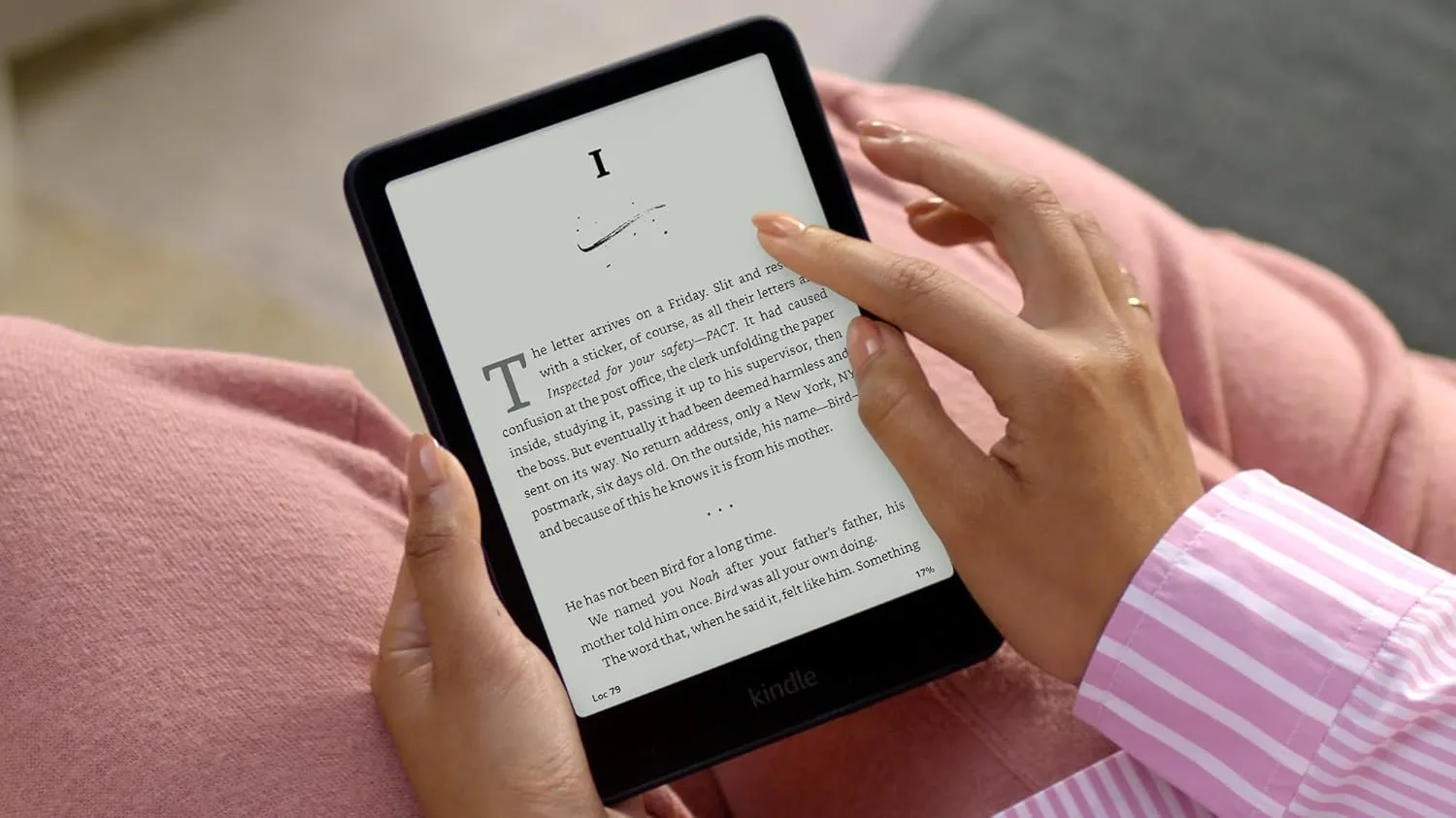 null Woman reading a Kindle Paperwhite with a black bezel, showing an e-book page, while wearing pink pants and a striped pink-and-white shirt.