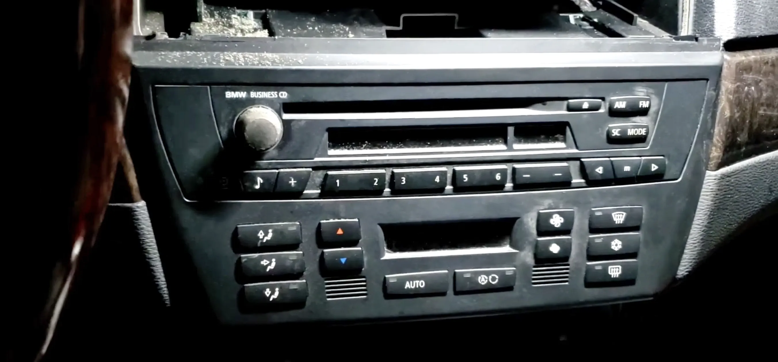 Close-up of a a BMW X3's in-dash car stereo with buttons, knobs, CD player slot, and air controls.