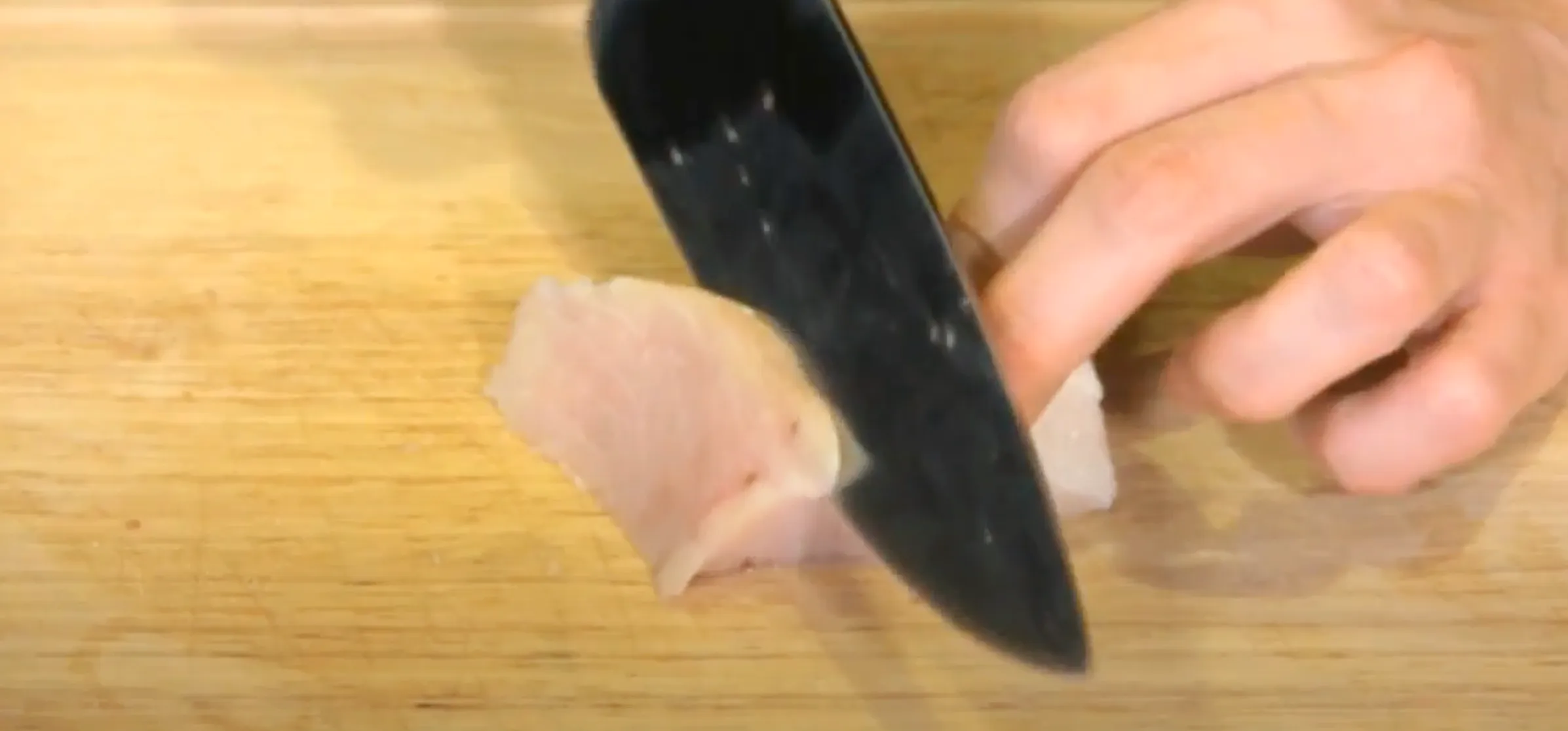 A knife slicing threw a piece of raw fish to make sashimi.