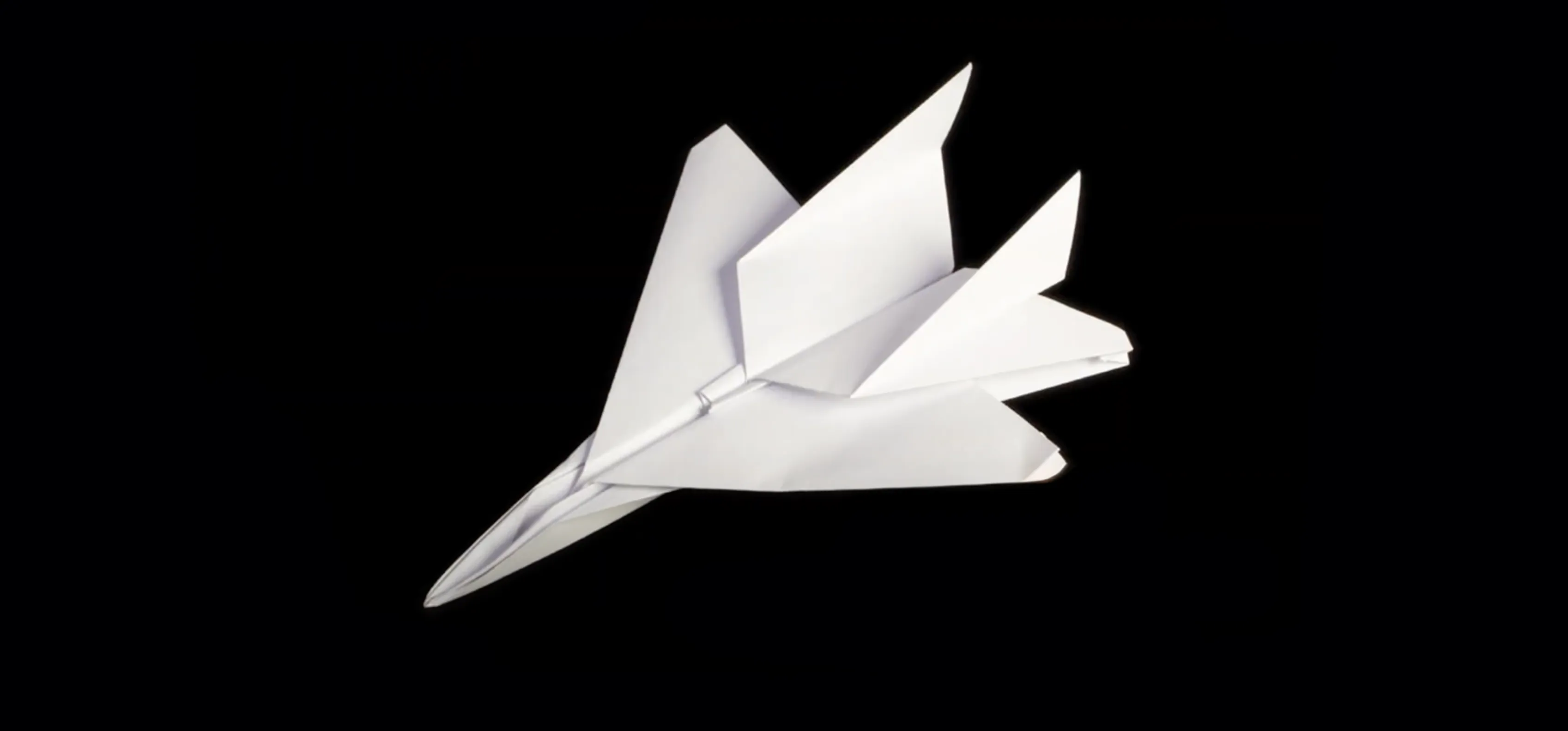 White F-15 jet fighter paper airplane with twin tails rests on black background, showcasing intricate folds and aerodynamic design.