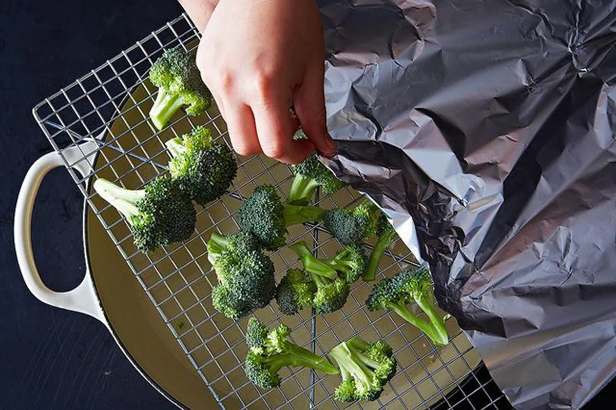 null Bird's-eye view of a pot with a wire cooling rack on top, with broccoli laying on it, about to be covered in foil.
