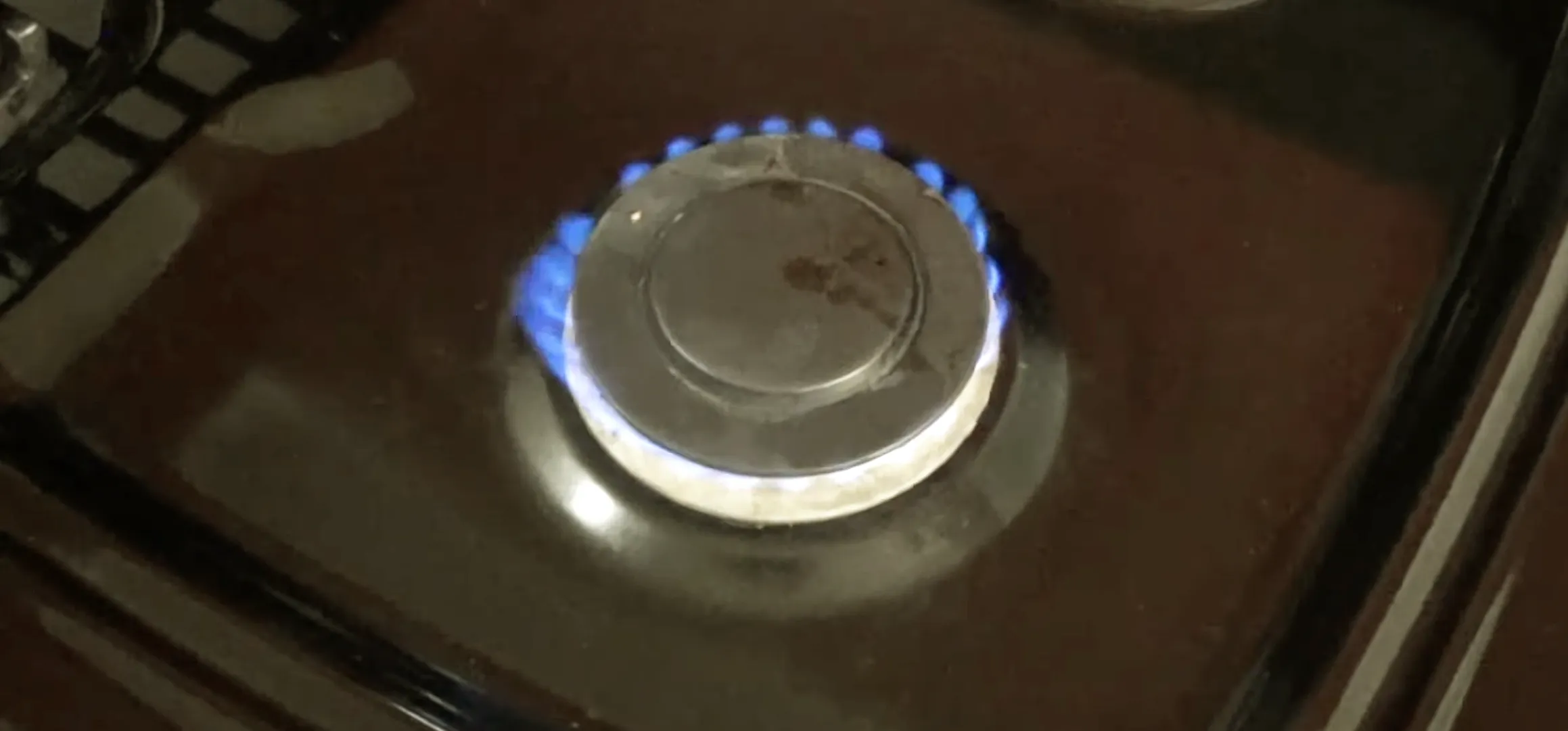 Blue flame ring encircles metal burner cap on glossy GE stovetop, illustrating lit gas range at low heat.
