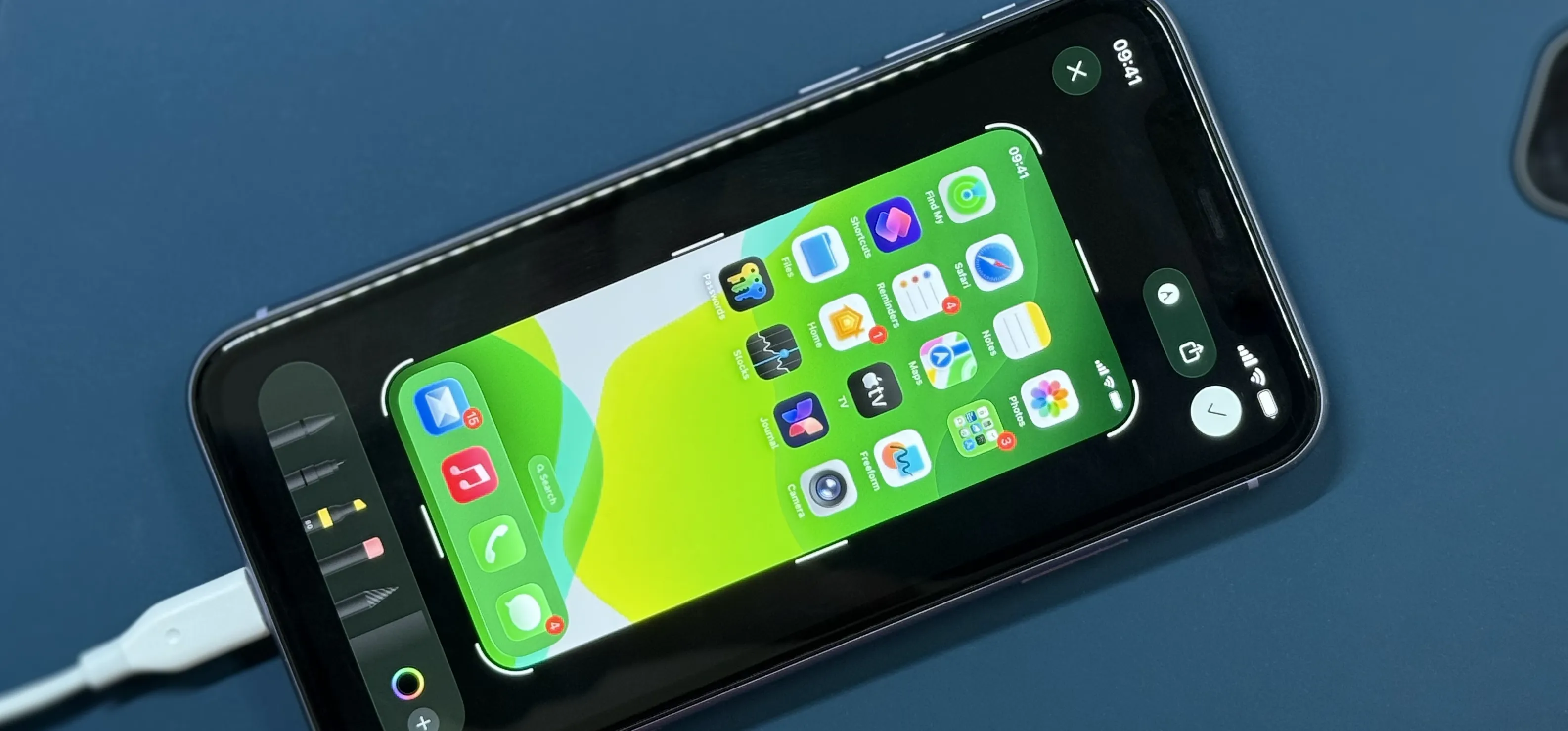 Landscape iPhone showing iOS screenshot markup tools over a green Home Screen thumbnail, Lightning cable attached, ready for editing.