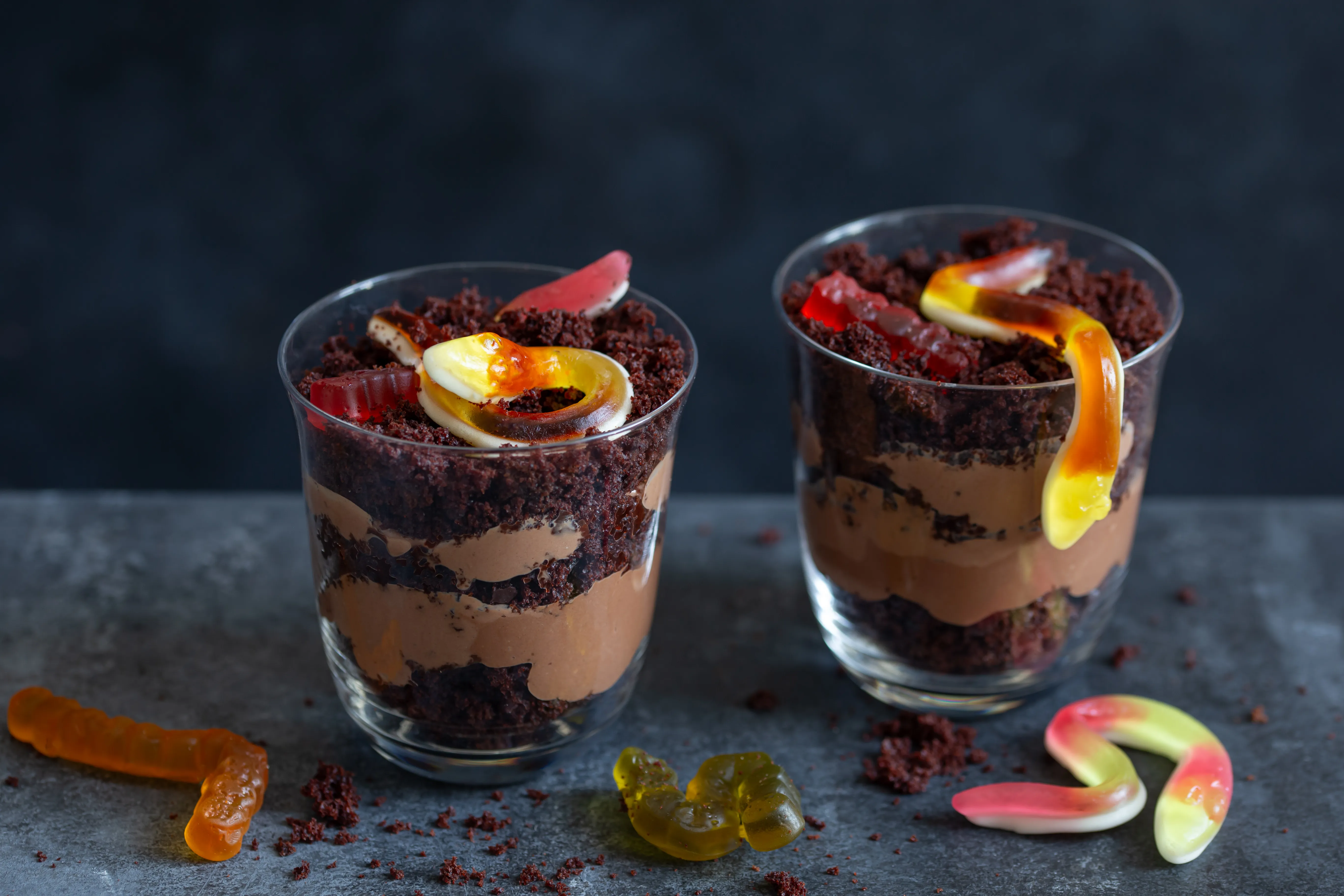 null Two clear cups with Oreo-based dirt and chocolate pudding levels and gummy worms inside and falling out onto the table.
