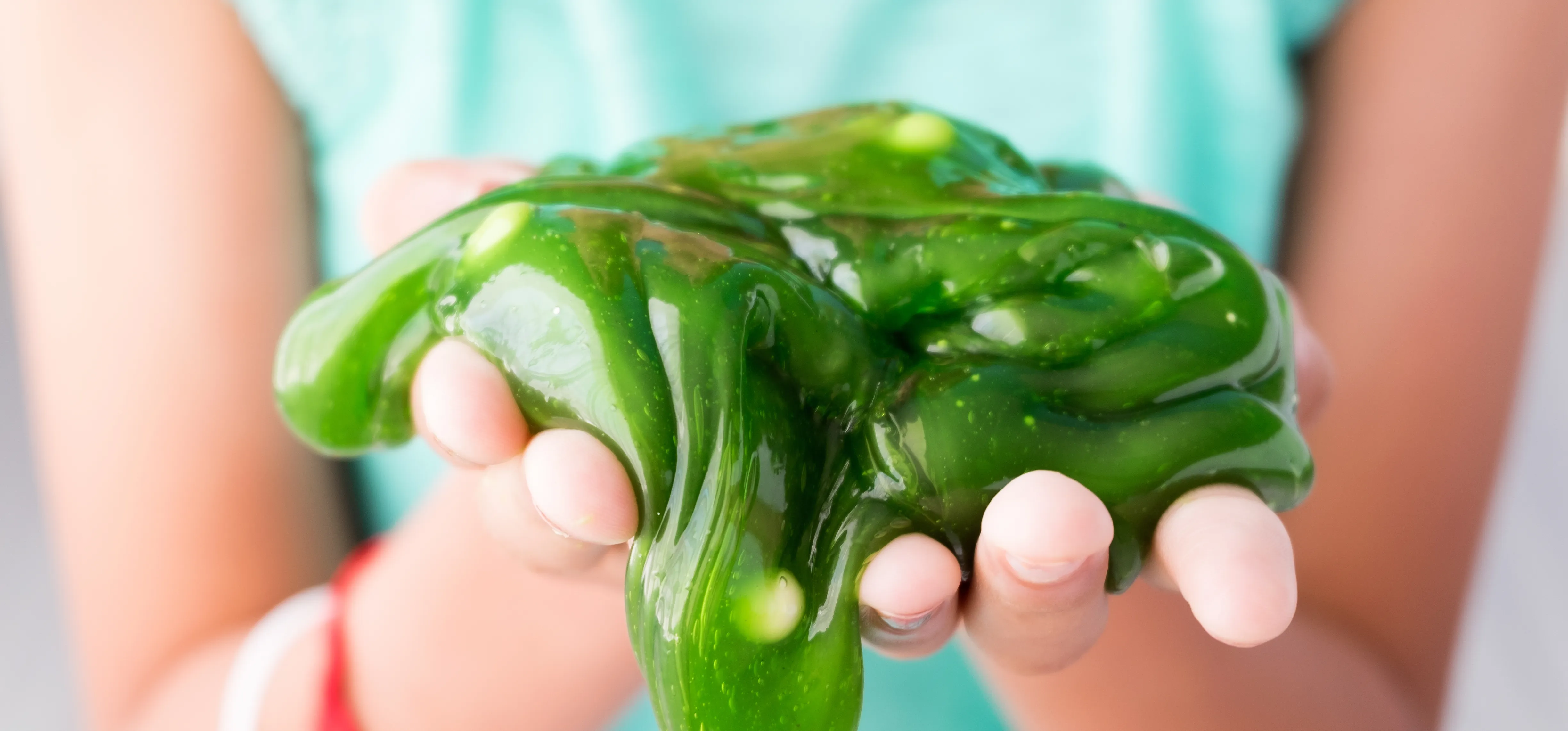 Closeup of the hands of a young child holding a goop of slimy green slime in her hands.