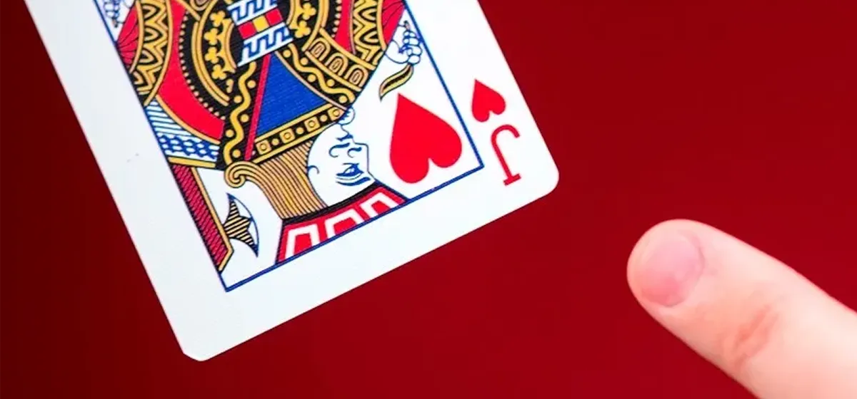 A finger pointing at a royal-looking Jack or Hearts playing card flying through the air with a red background.