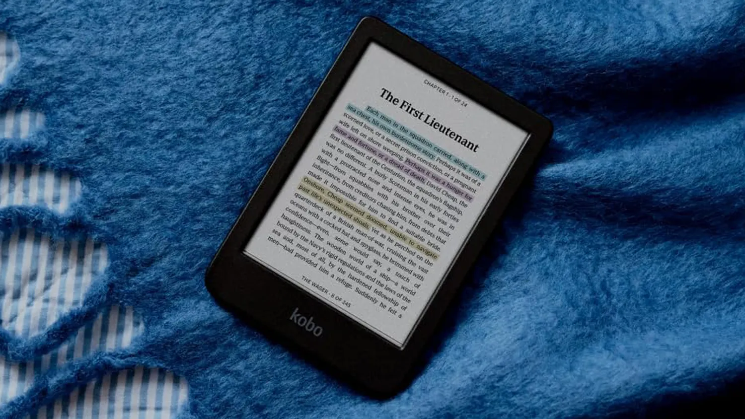 null Kobo Clara Colour e-reader displaying a chapter with highlighted text in blue, pink, and yellow, resting on a soft blue blanket with striped fabric peeking through.