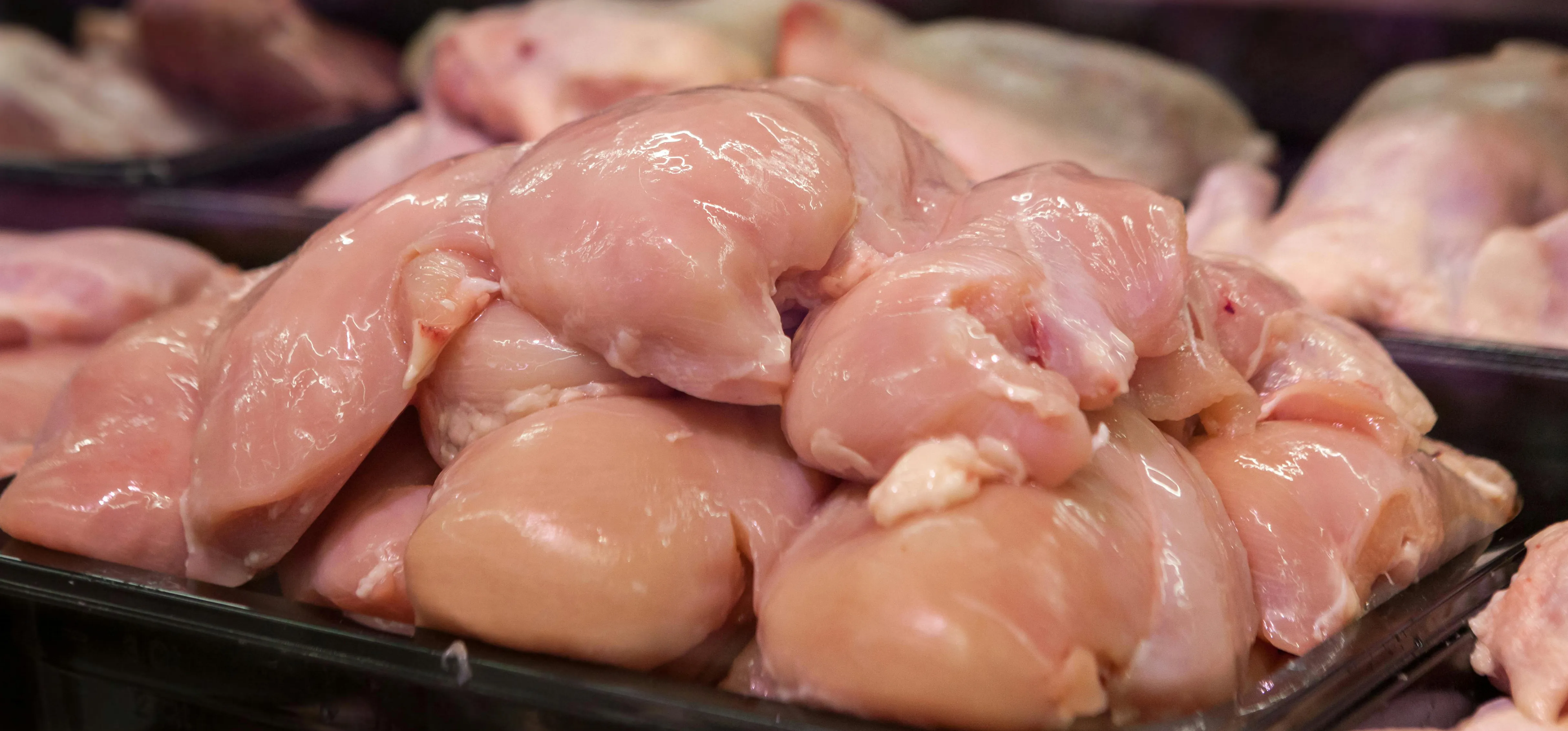 A pile or raw chicken breasts on a black scale in a grocery store.