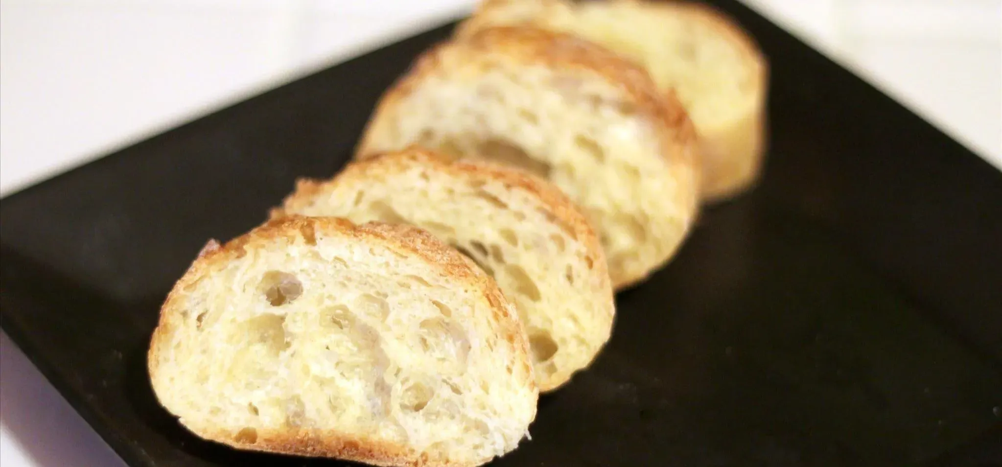 Sliced French baguette bread on a black plate.