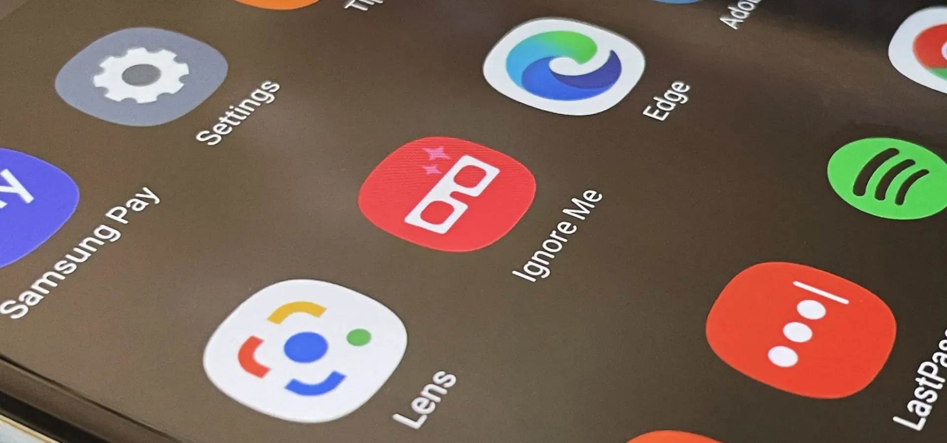 Close-up of a Samsung Galaxy phone screen showing the “Ignore Me” app icon with white 3D glasses on a red background among other familiar apps like Settings, Lens, Edge, and Spotify.
