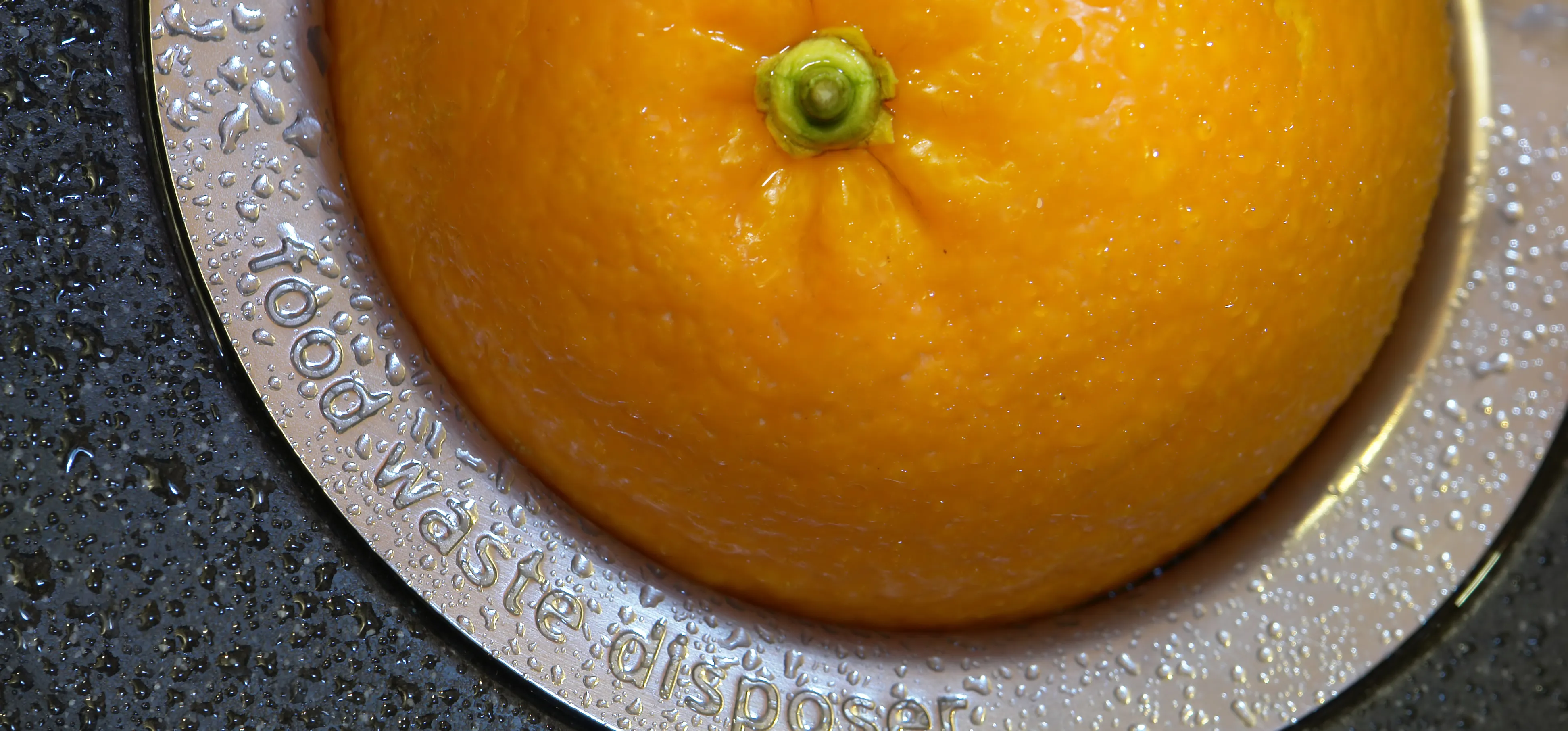 An orange stuck in a garbage disposal drain in a kitchen sink.