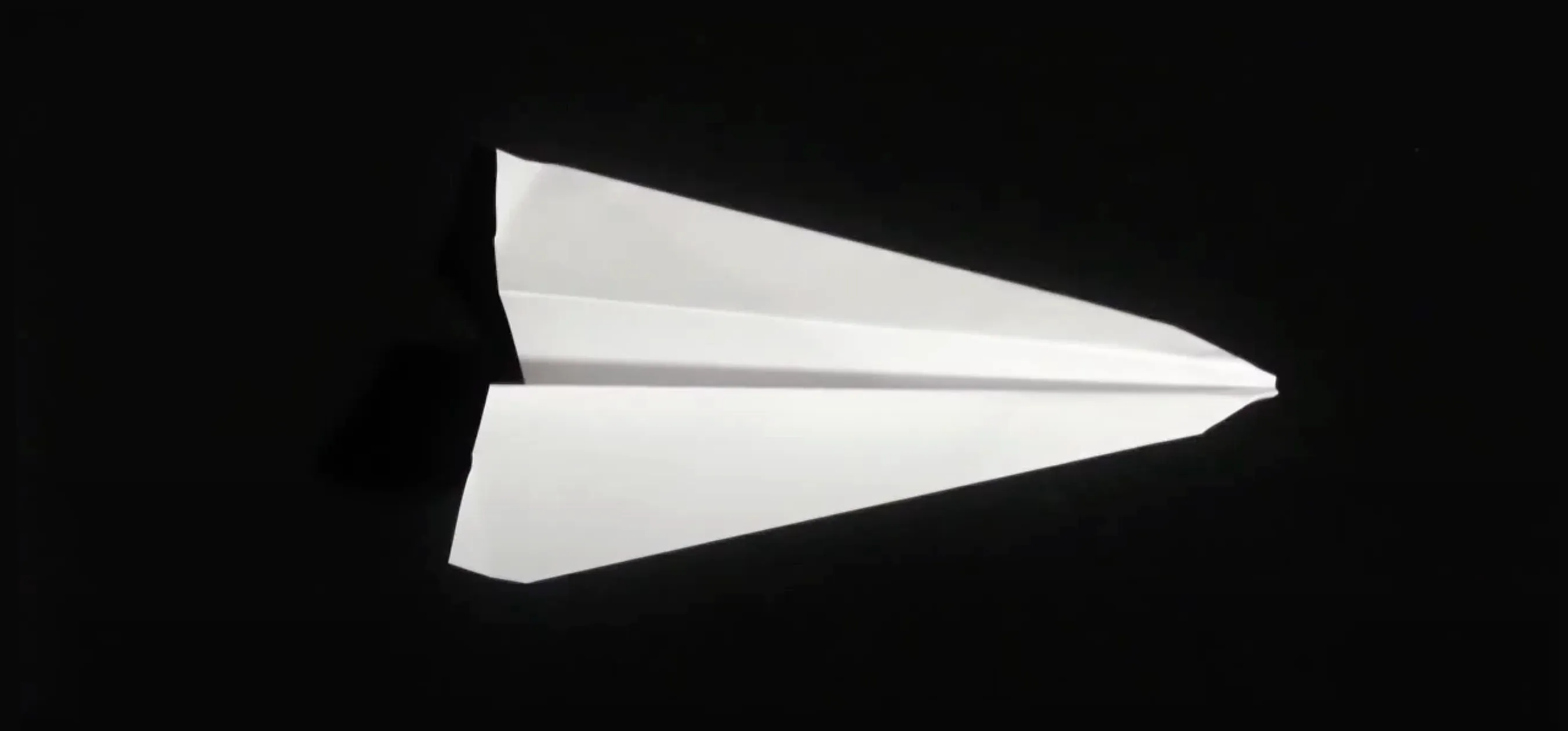 White Super Arrow paper airplane with tapered wings lies against black background, sharp nose emphasizing long-distance flight design.