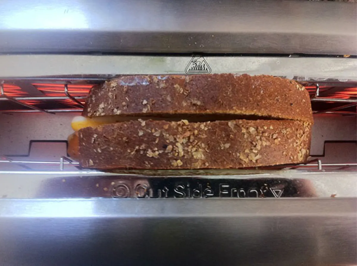 null A whole cheese sandwich stuffed inside one slot of a regular toaster with the heating elements aglow.
