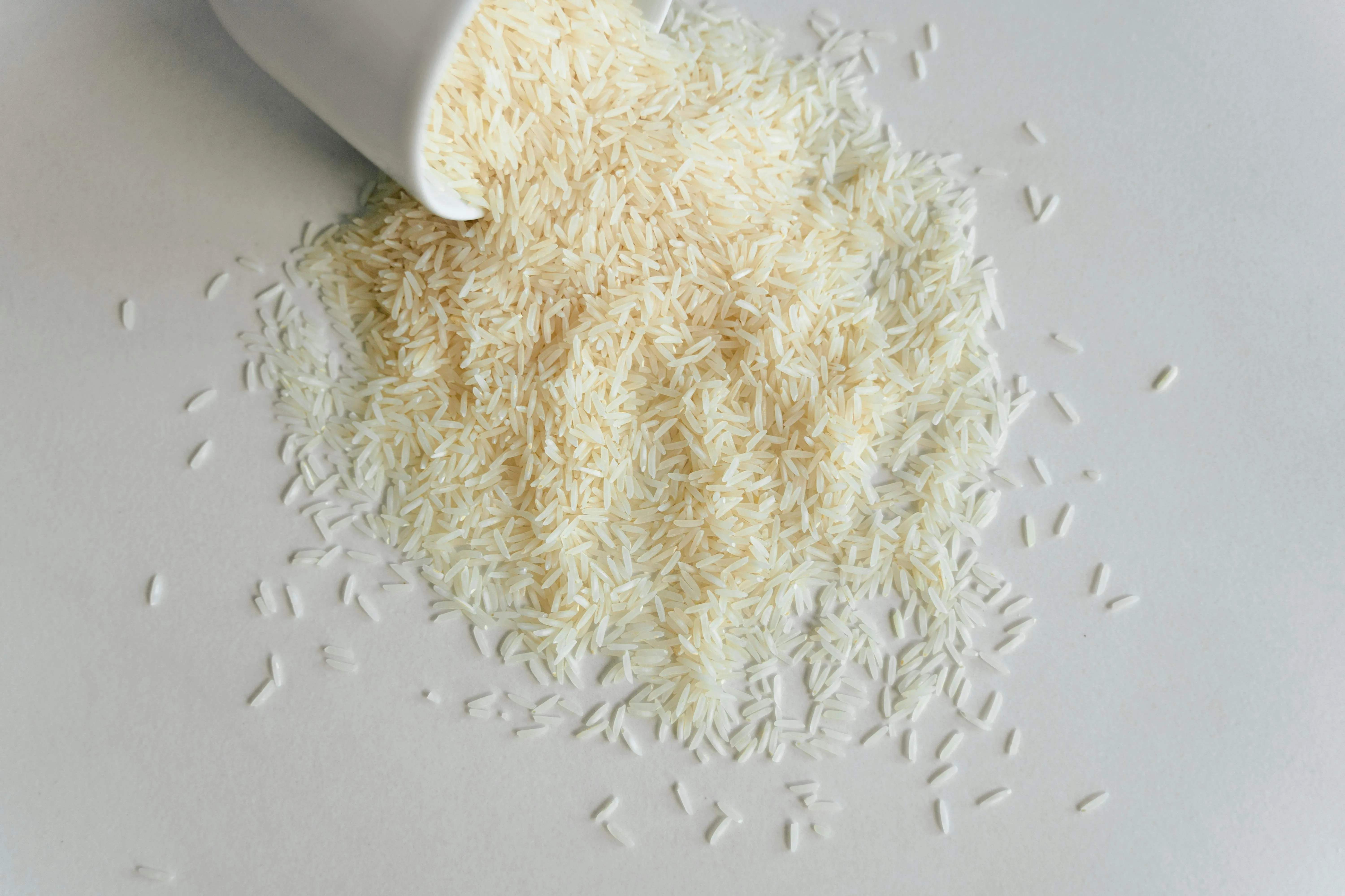 null Uncooked white rice spilling out of a white mug on a white table.